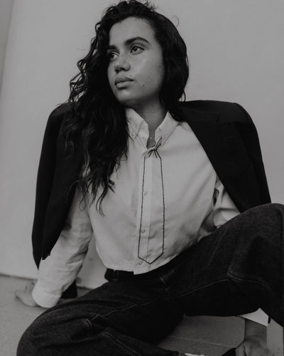 Female sitting on the floor wearing a white shirt, dark jacket, and jeans.