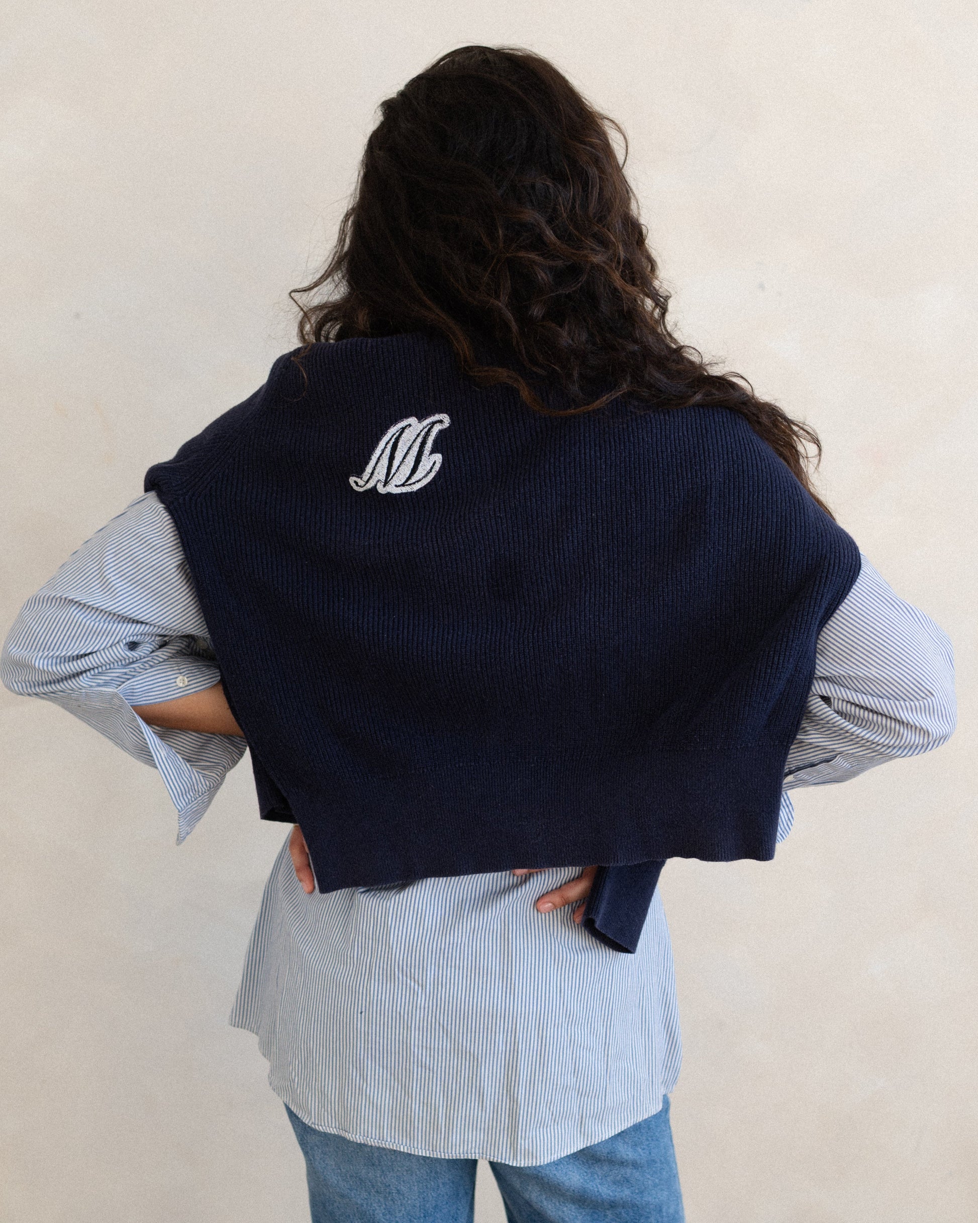 Person wearing a navy blue vest with a logo on the back, standing against a plain background.