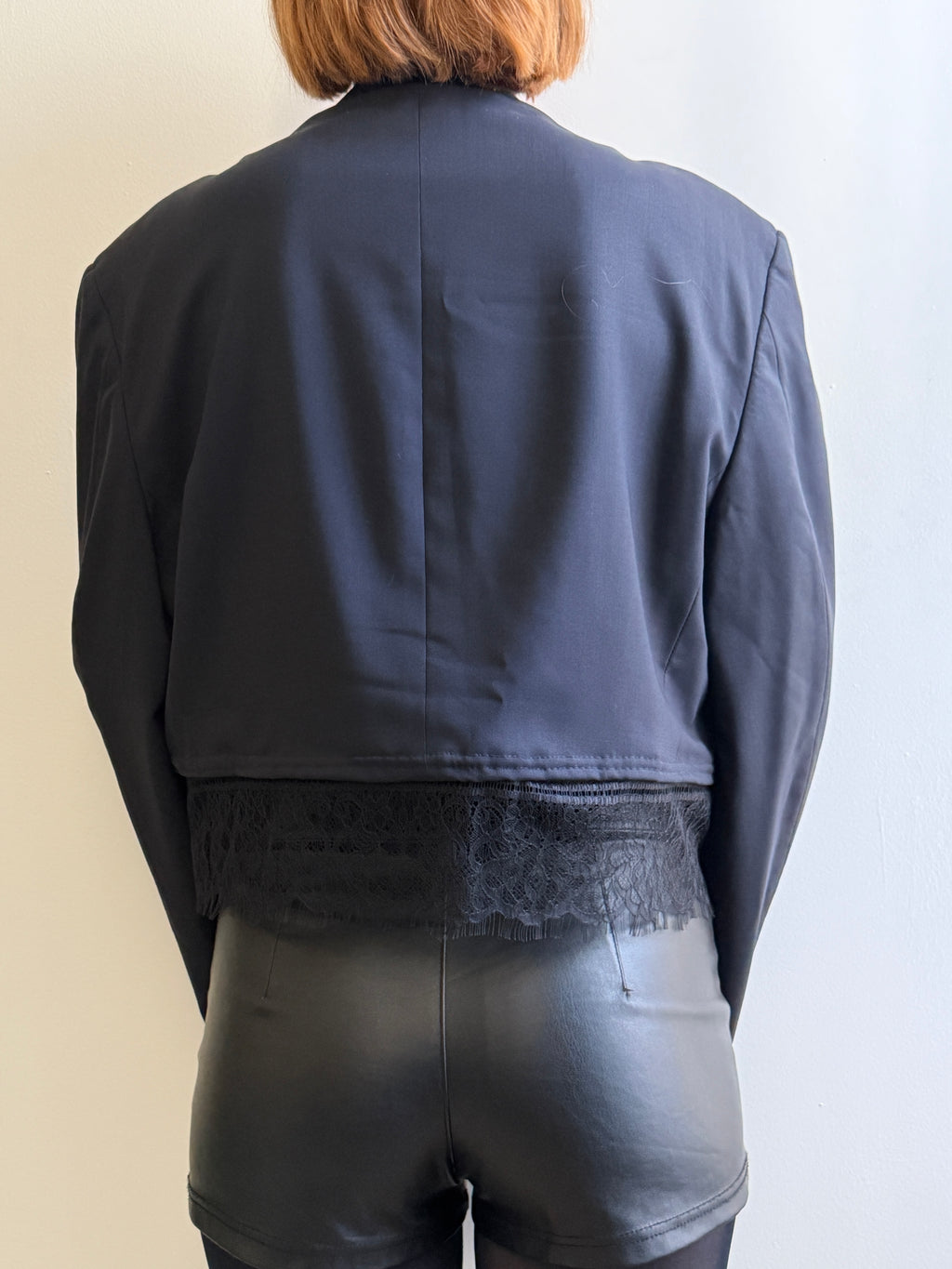 Person wearing a dark blue jacket with a lace detail on the back, standing against a plain background.