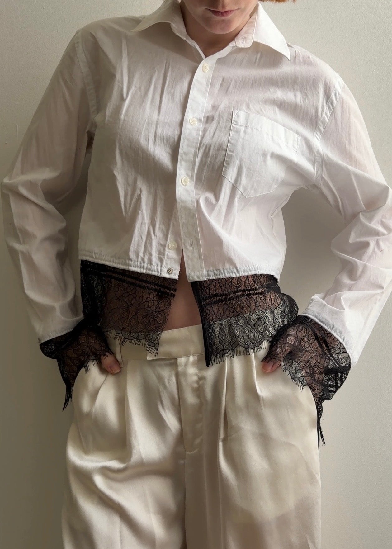 Person wearing a white shirt with lace cuffs and a plain background