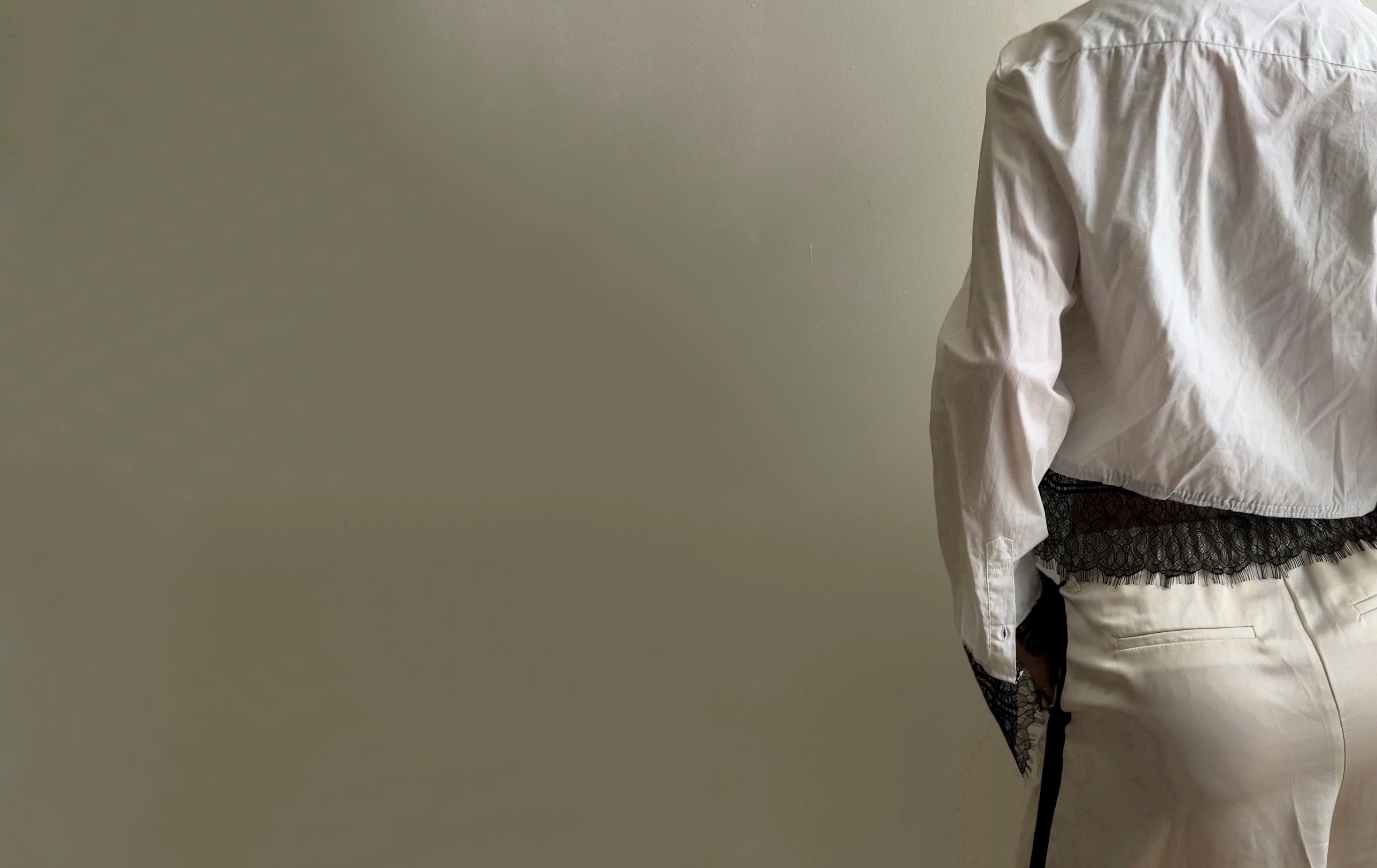Person wearing a white shirt and black belt against a plain wall