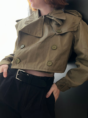 Female wearing a cropped green trench coat with a dark background