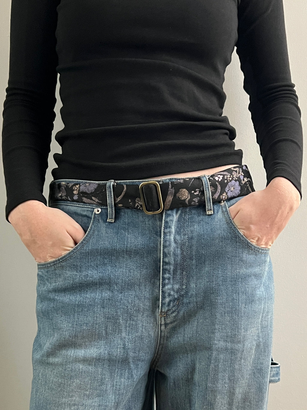 Person wearing a black long-sleeve shirt and blue jeans with a patterned belt.