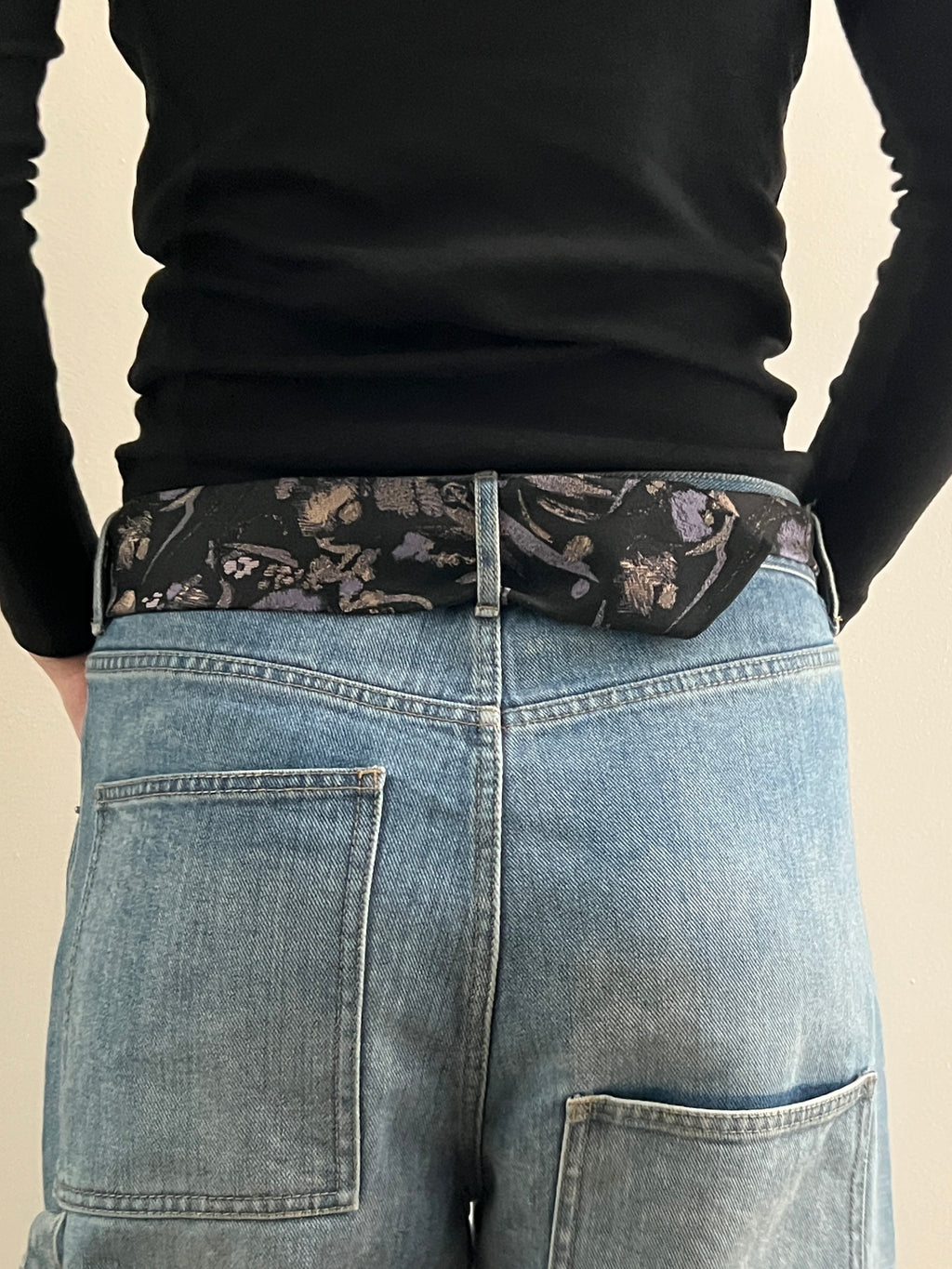 Person wearing a black long-sleeve shirt and blue jeans with a floral belt.