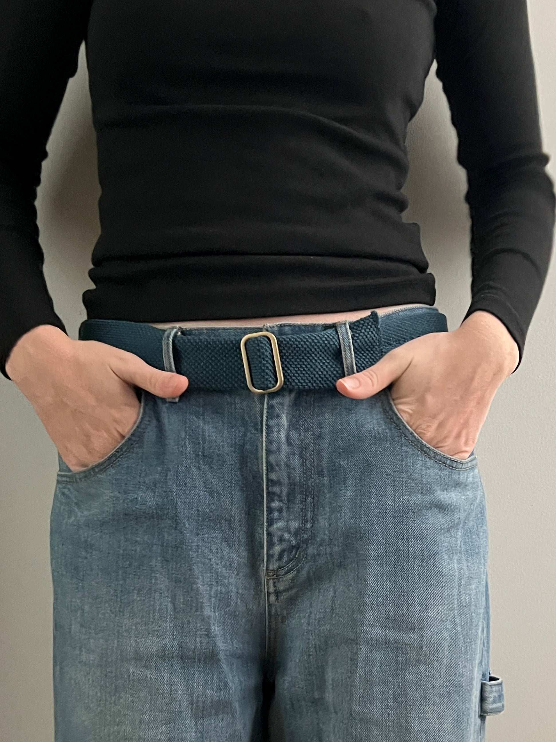 Person wearing a black long-sleeve top and blue jeans with a green belt.