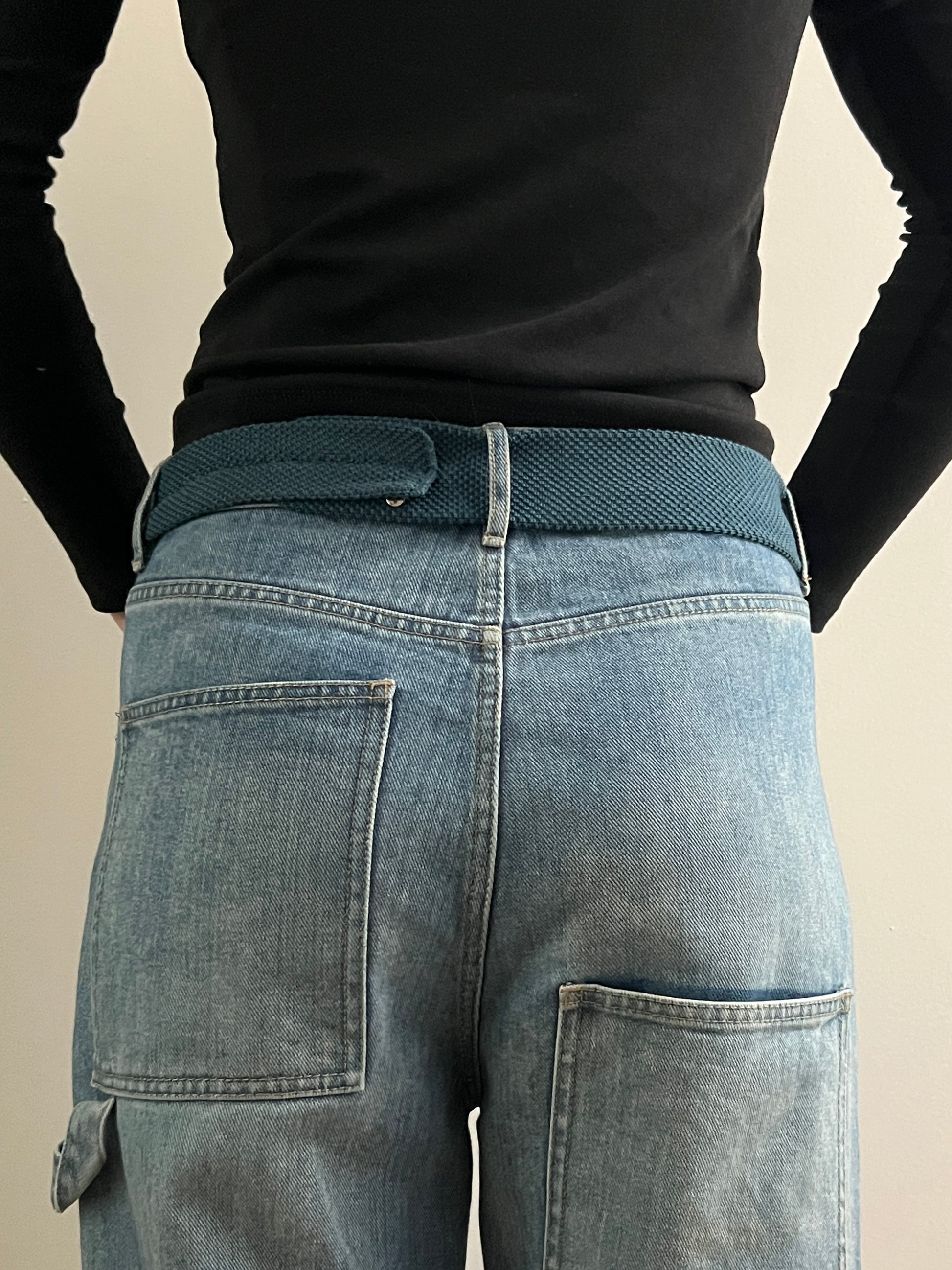 Person wearing a black long-sleeve top and blue jeans with a green belt.