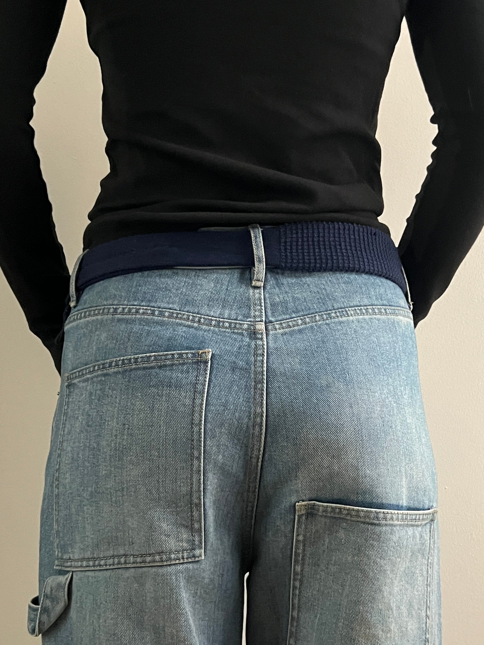 Person wearing a black long-sleeve shirt and blue jeans on a beige background