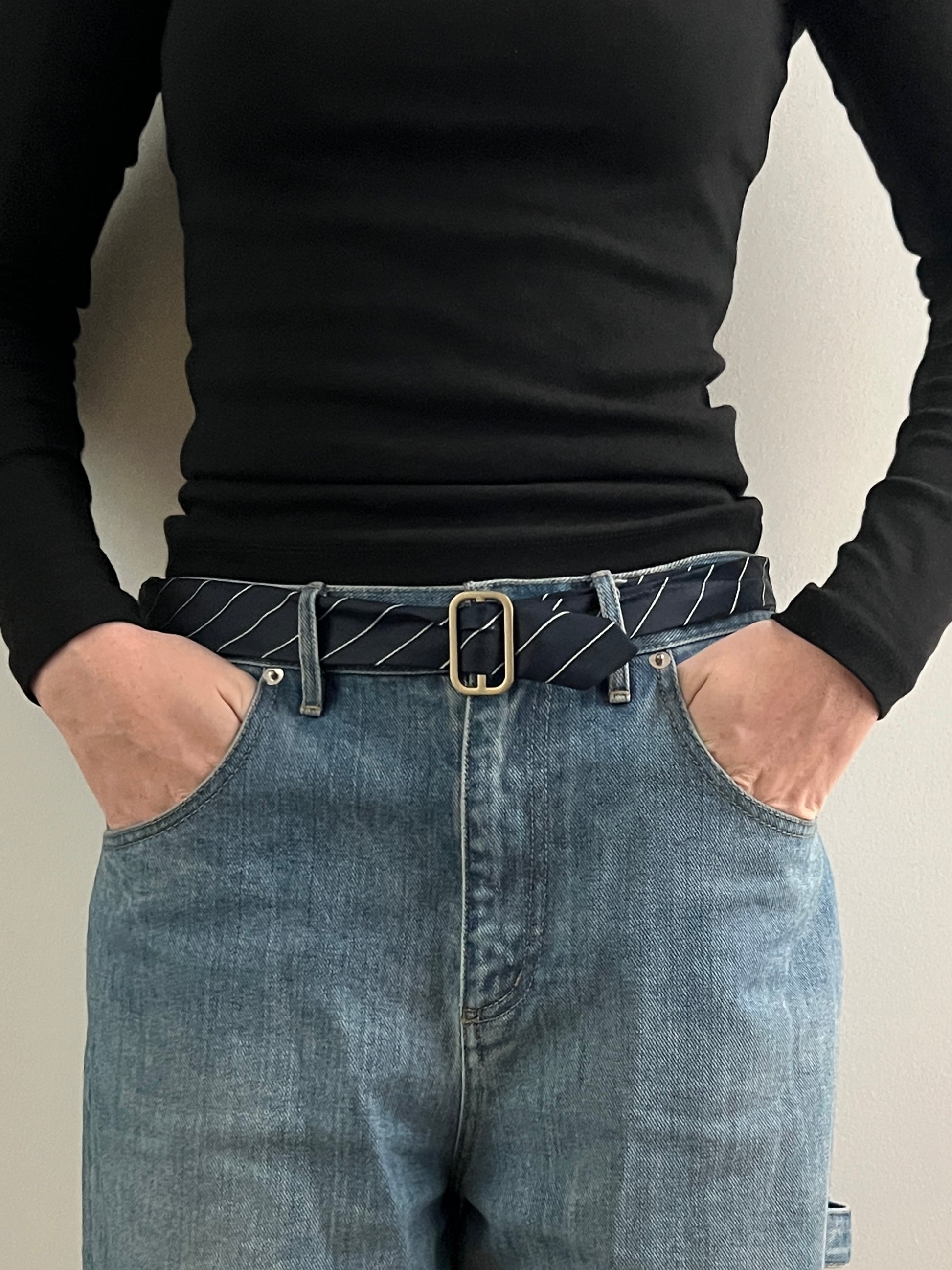 Person wearing a black long-sleeve shirt and blue jeans with a belt.