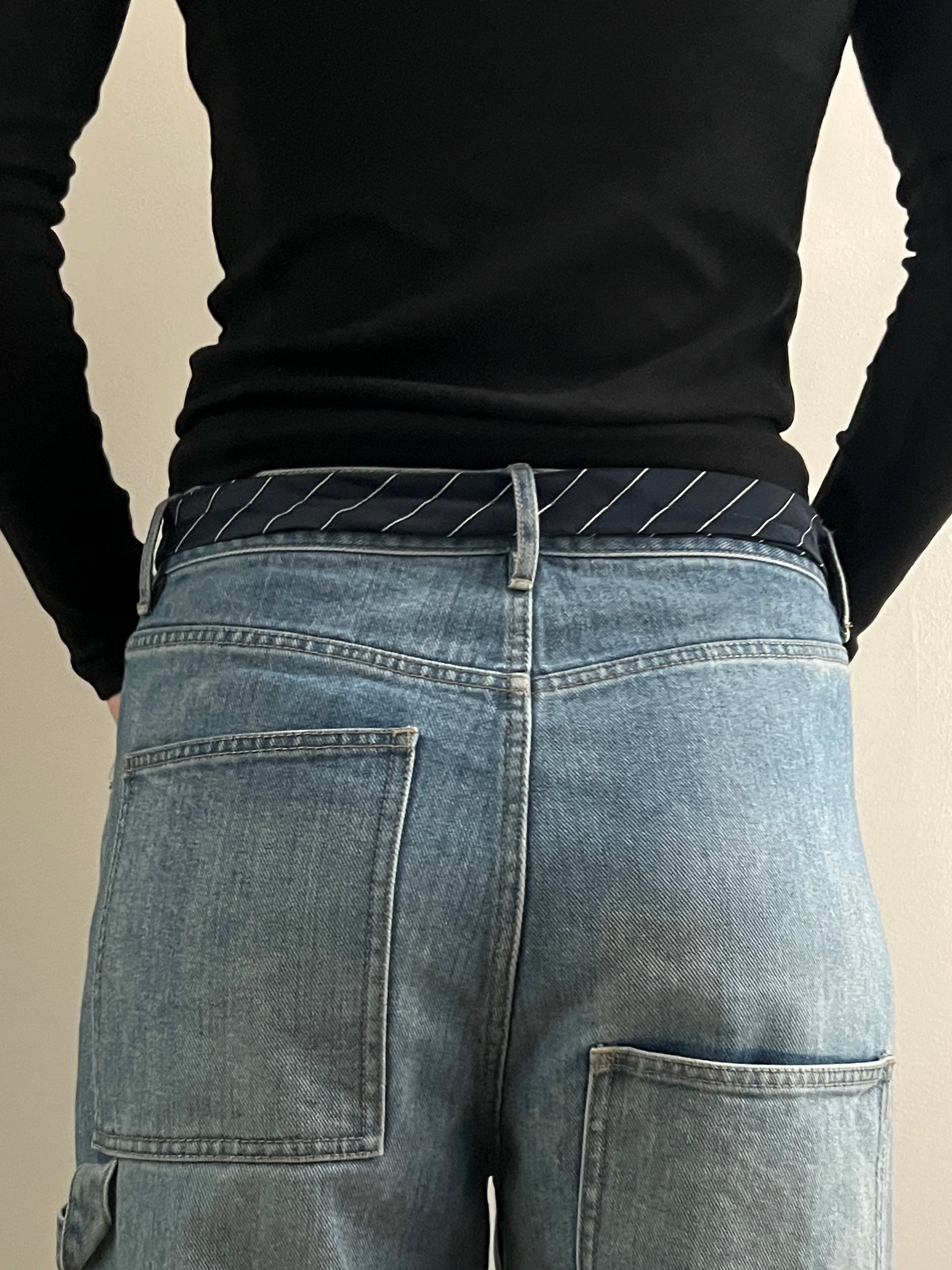 Person wearing blue jeans and a black long-sleeve shirt on a beige background