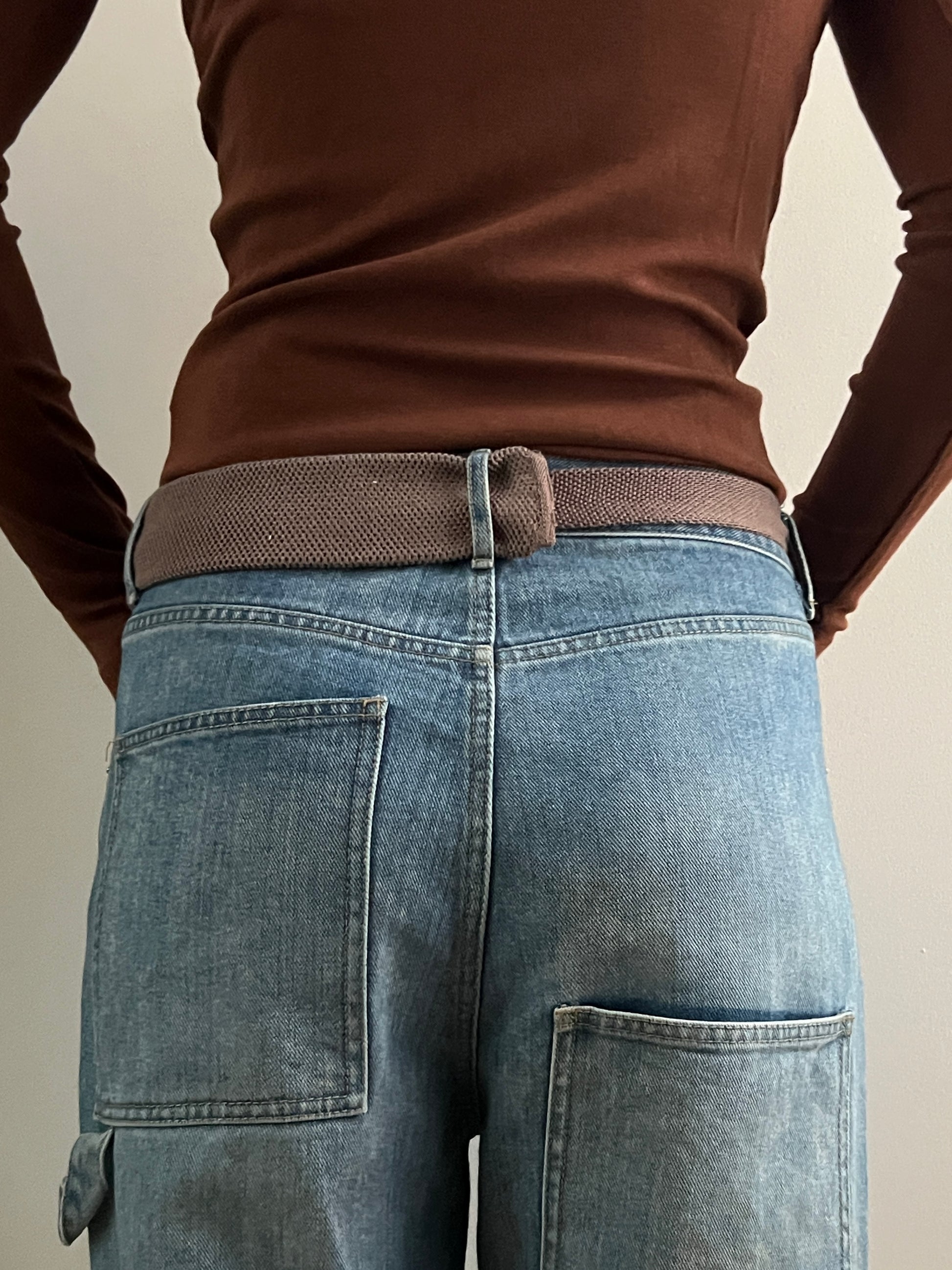 Person wearing blue jeans and a brown shirt with a neutral background