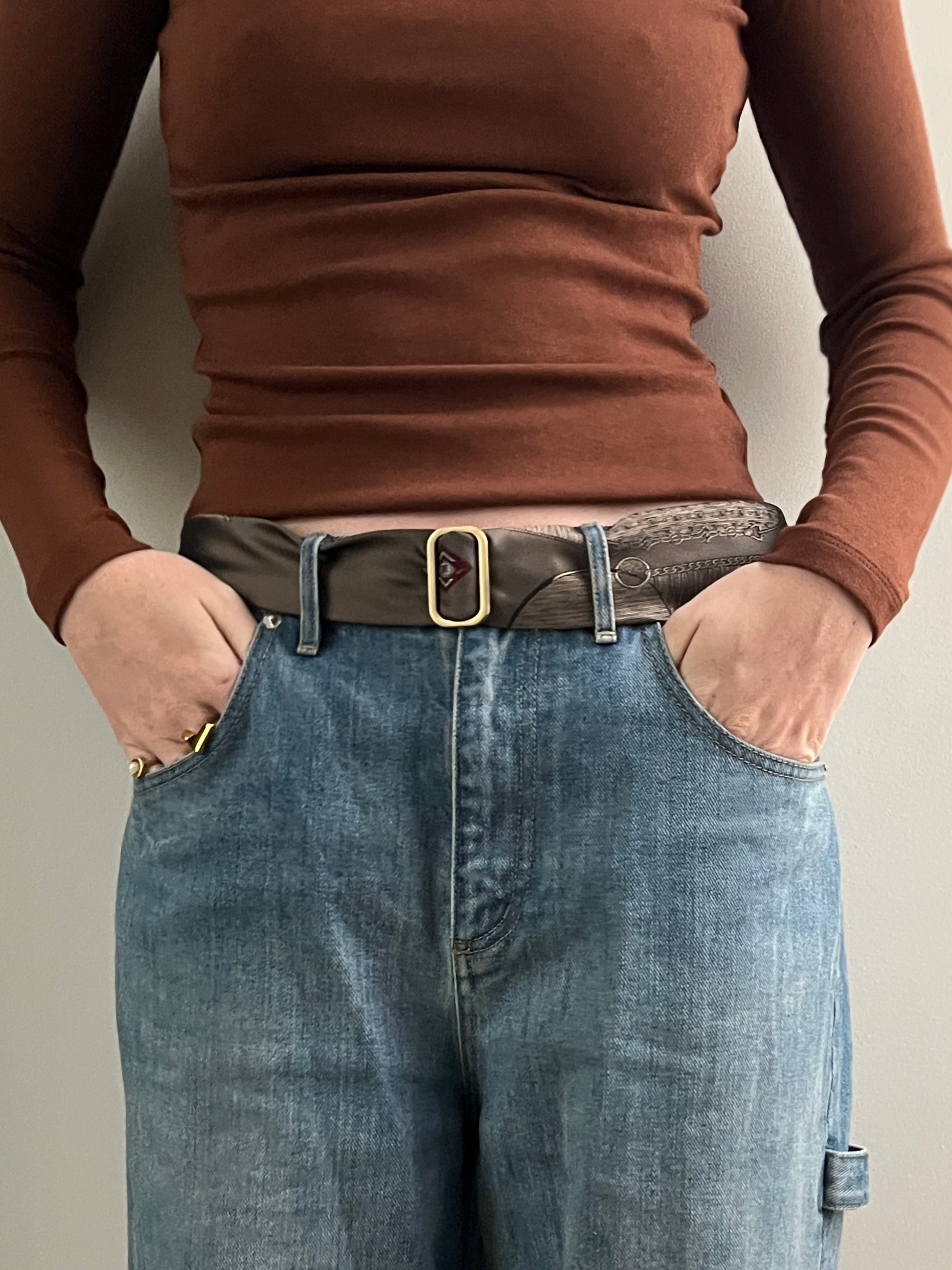 Person wearing a brown long-sleeve shirt and blue jeans with a belt.
