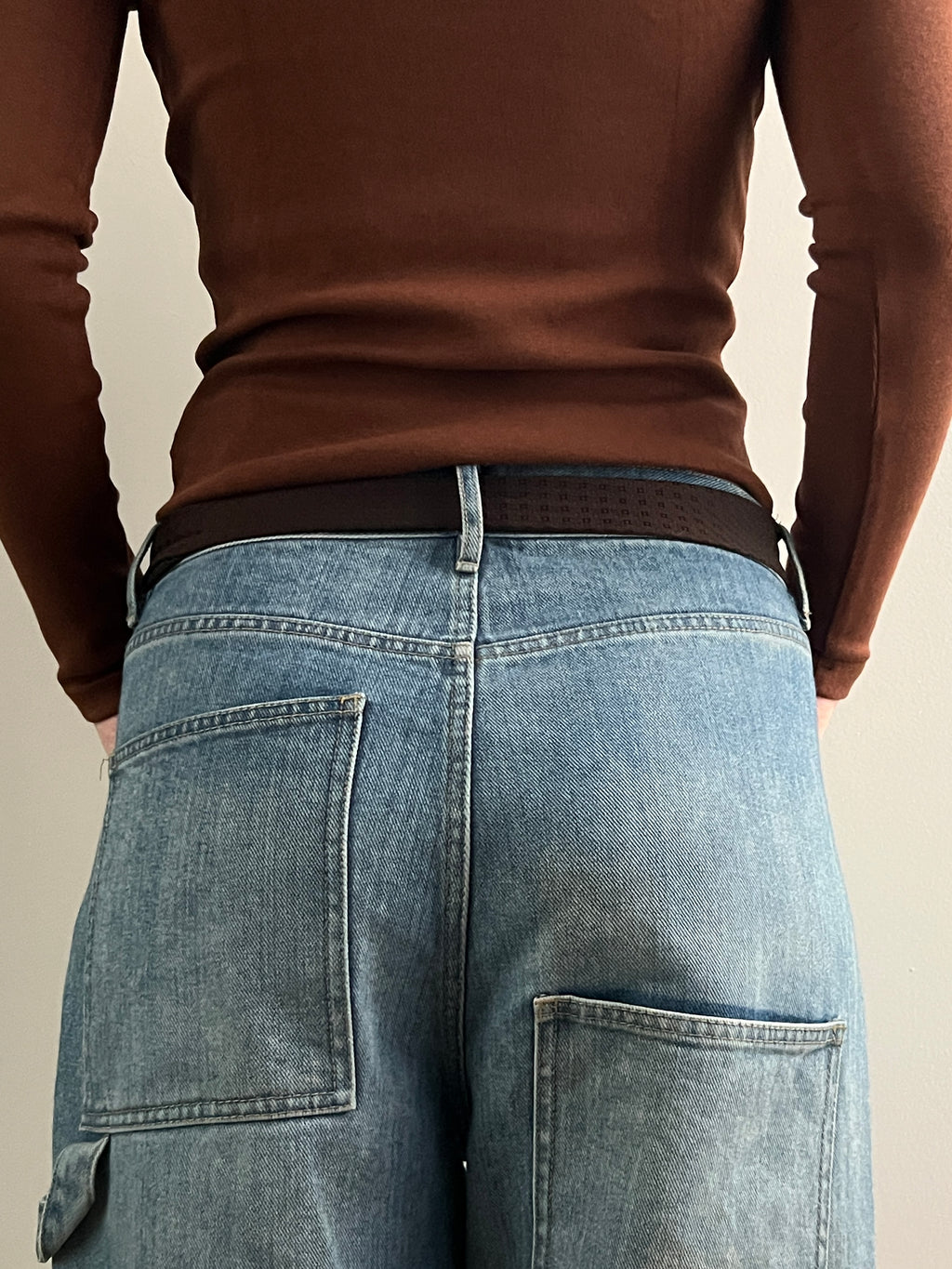 Person wearing a brown sweater and blue jeans with a neutral background