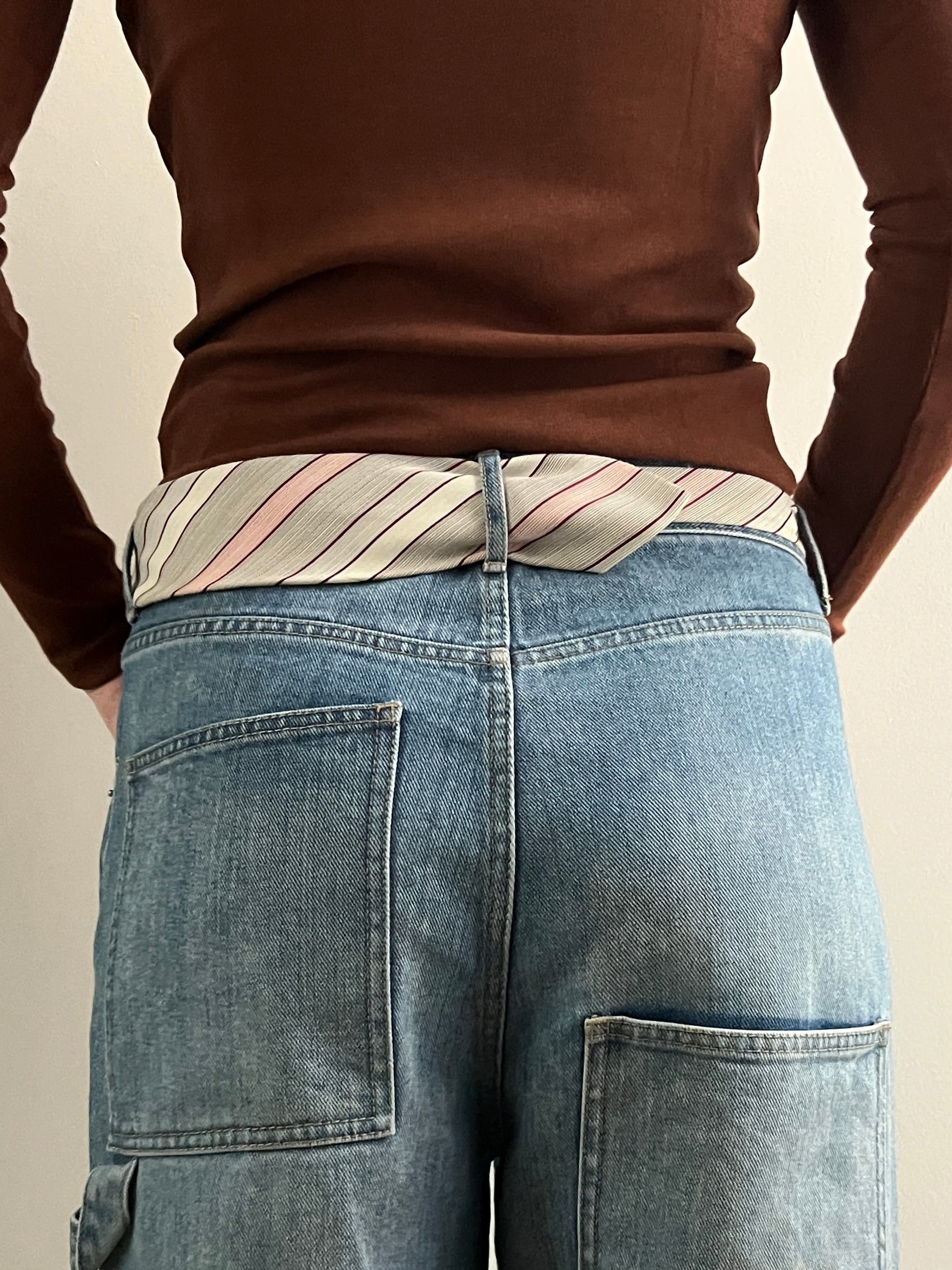 Person wearing a brown long-sleeve shirt and blue jeans with a striped belt.