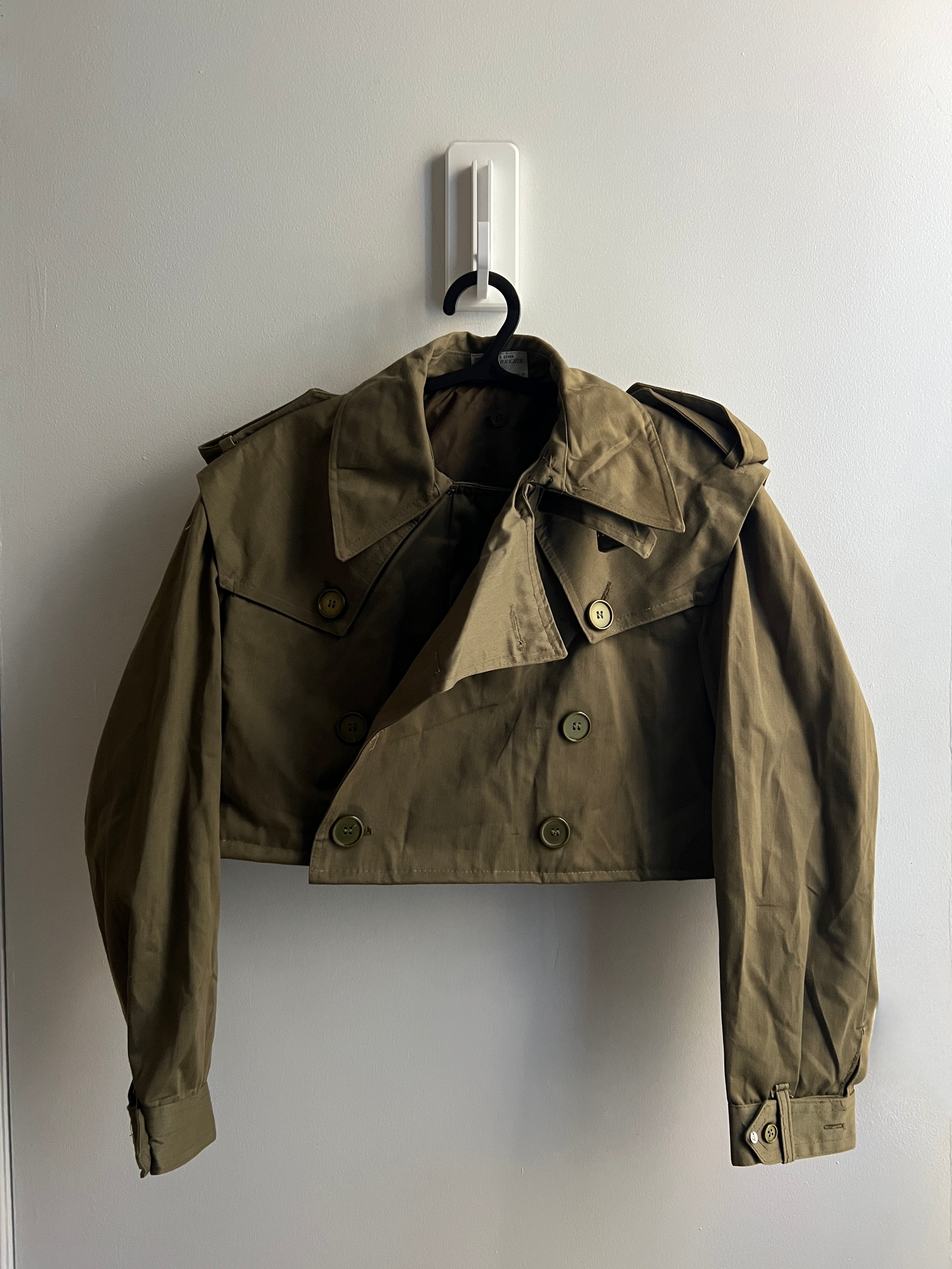 Green cropped trench jacket on a hanger against a white wall
