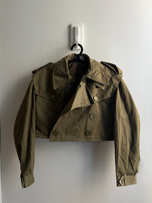 Green cropped trench jacket on a hanger against a white wall
