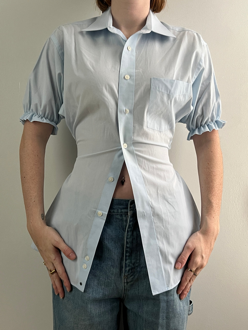 Female wearing a pale blue short sleeve puff sleeve button down blouse with a cinched back facing front.