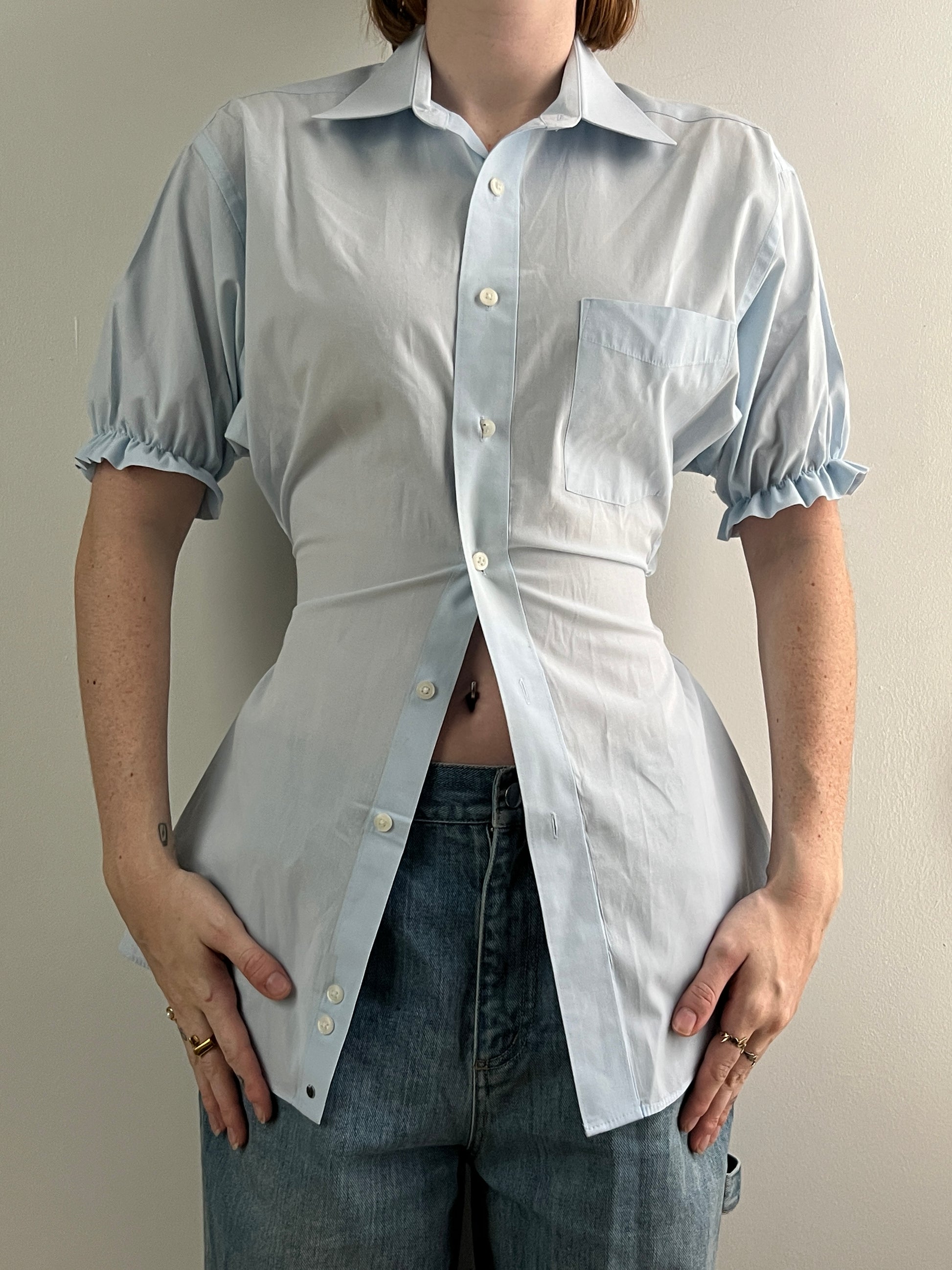 Female wearing a pale blue short sleeve puff sleeve button down blouse with a cinched back facing front.