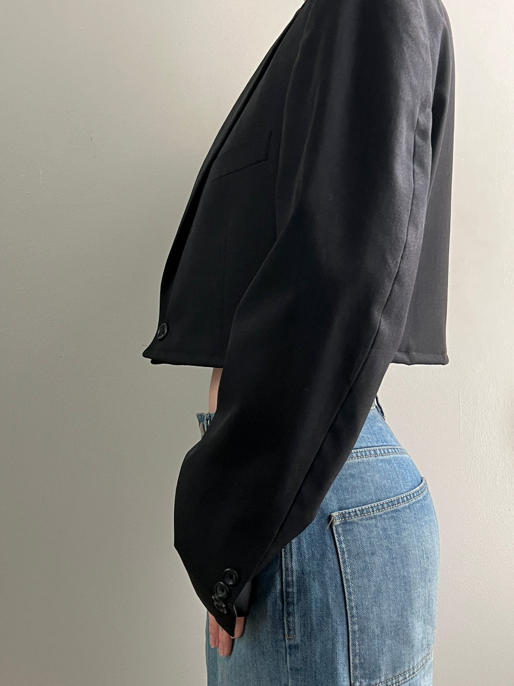 Cropped black blazer draped over a person wearing blue jeans on a neutral background