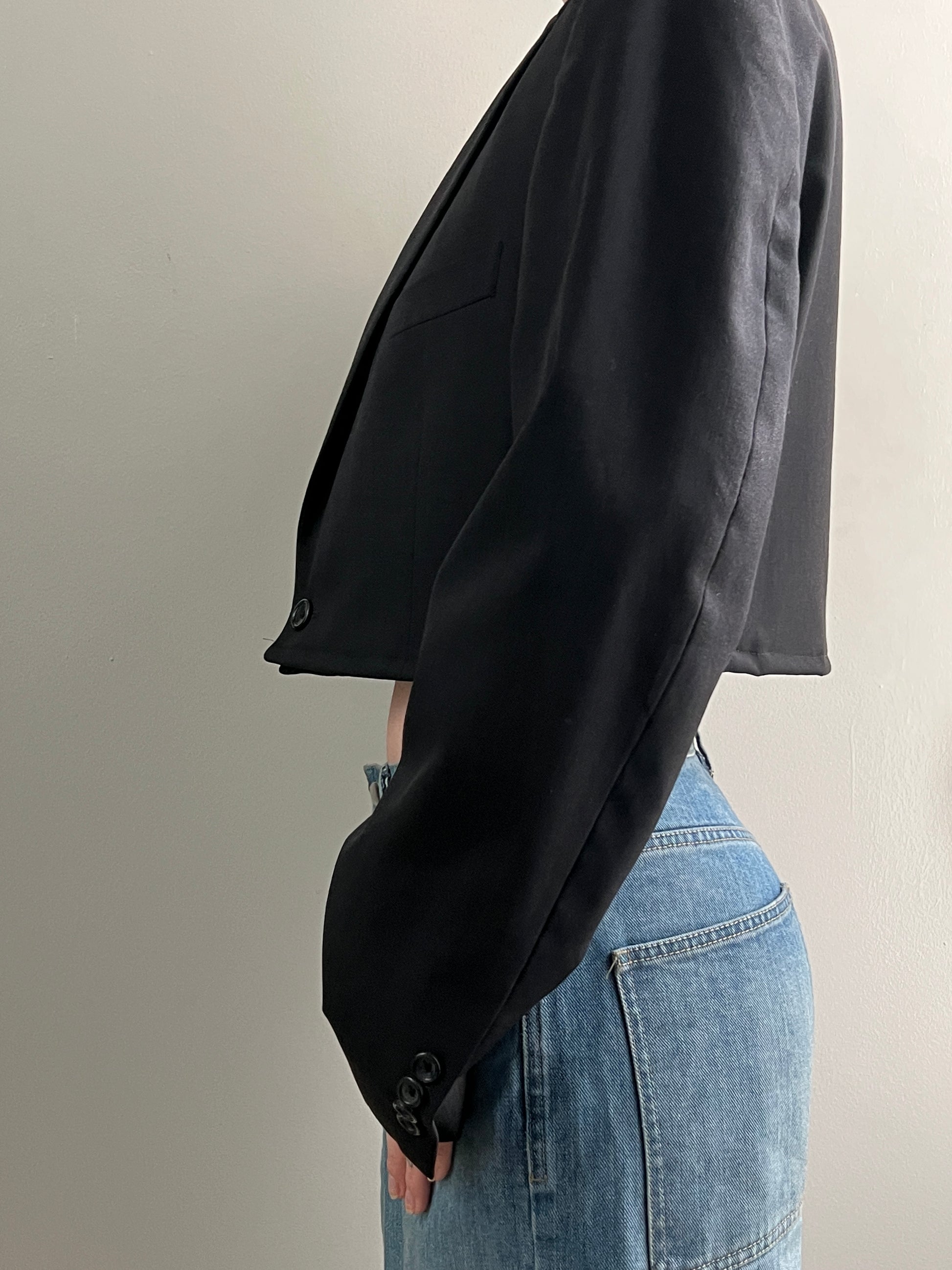 Cropped black blazer draped over a person wearing blue jeans on a neutral background
