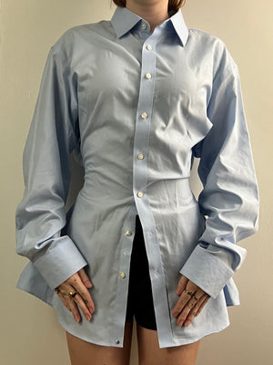 Female wearing a blue button down blouse with a cinched back facing front.