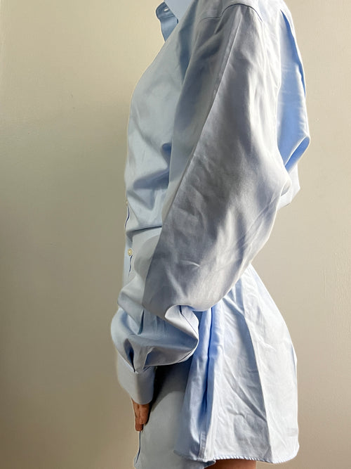 Female wearing a white button down blouse with a cinched back facing left.