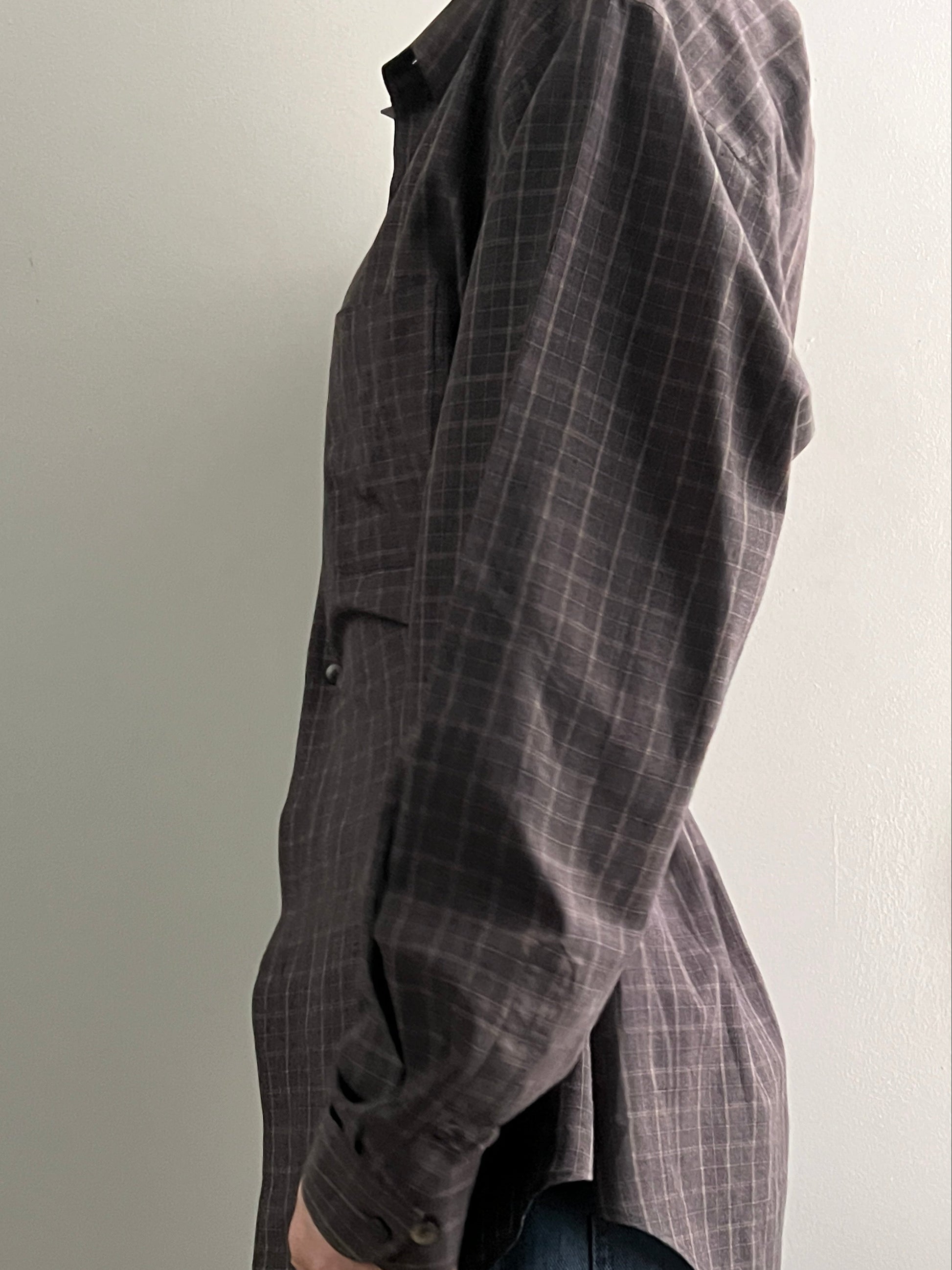 Female wearing a brown checkered long sleeve button down blouse with a neutral background facing the left.