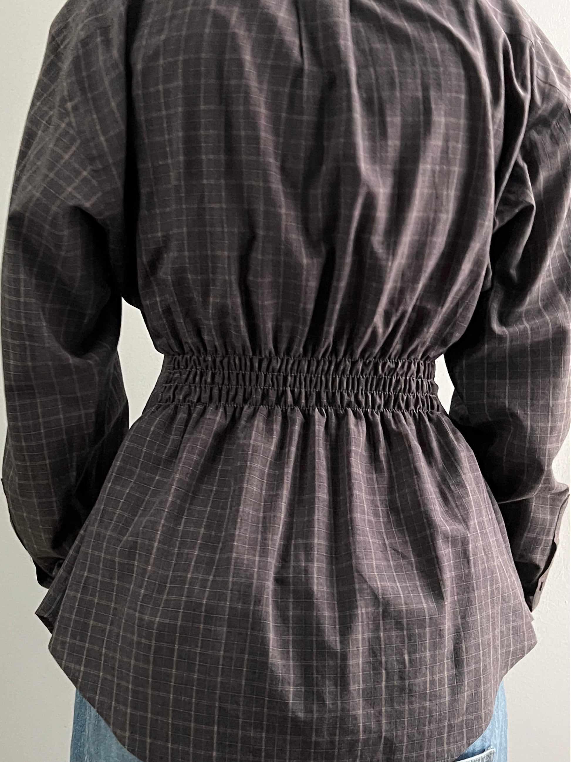 Female wearing a brown checkered long sleeve button down blouse featuring the elastic back with a neutral background.