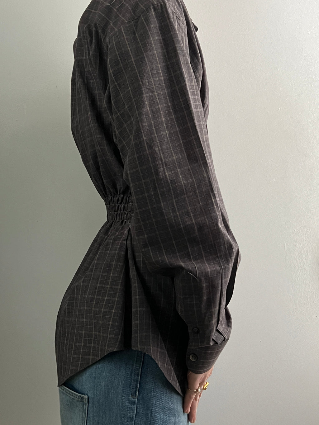 Female wearing a brown checkered long sleeve button down blouse with a neutral background facing the right
