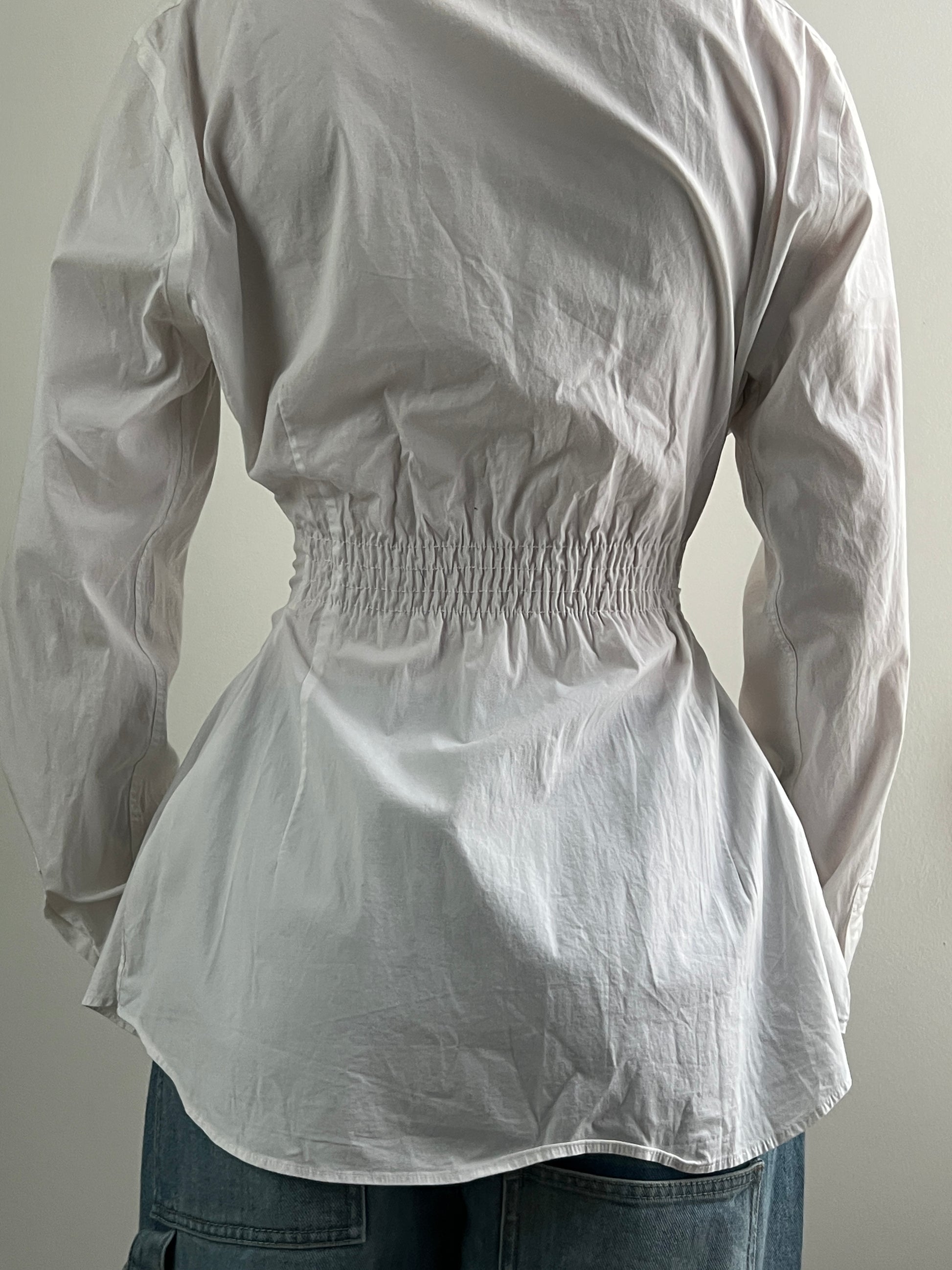 Female wearing a white navy nautically embroidered button down blouse with a cinched elastic back facing back.