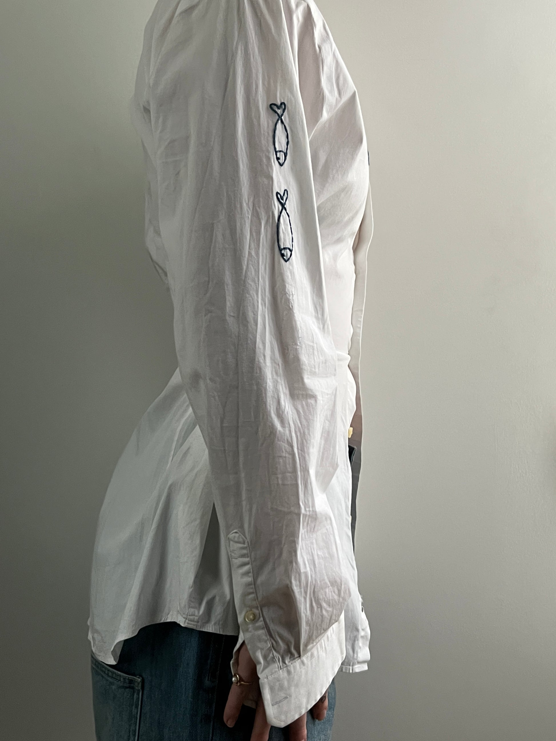 Female wearing a white navy nautically embroidered button down blouse with a cinched elastic back facing right.