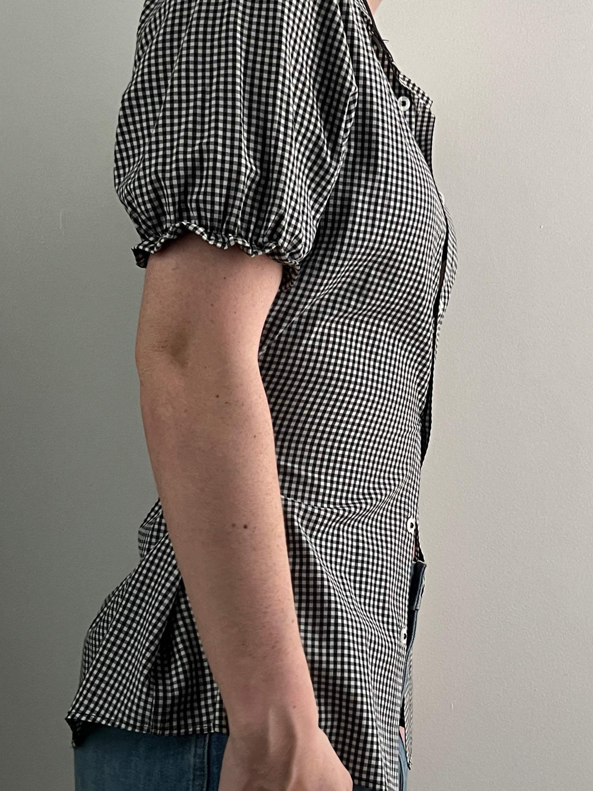 Female wearing a black and white checkered shirt with puff sleeves and jeans.