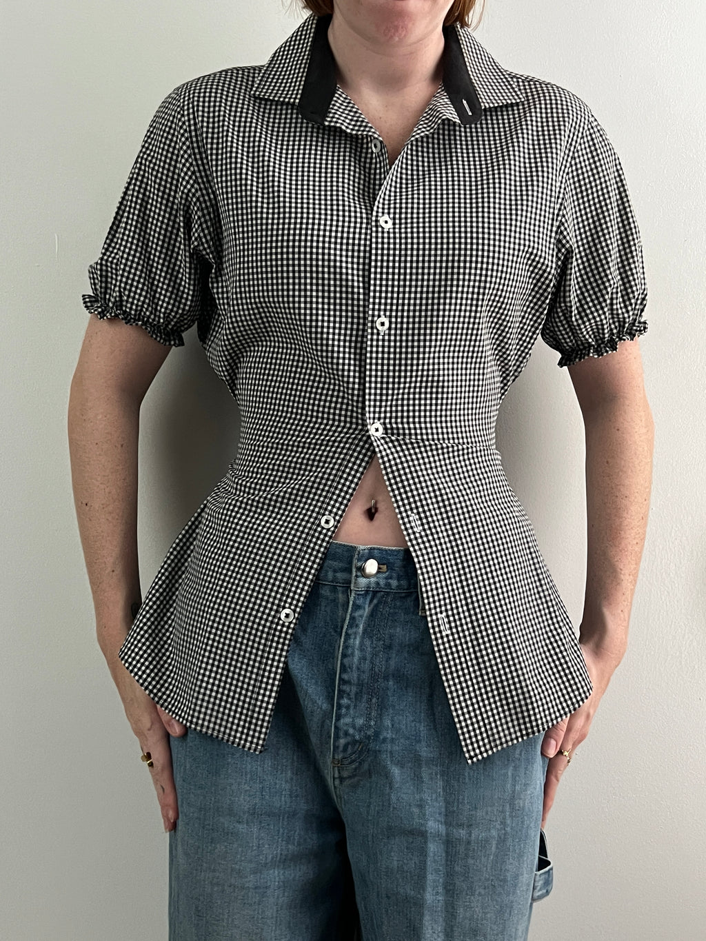 Female wearing a black and white checkered shirt with puff sleeves and jeans.