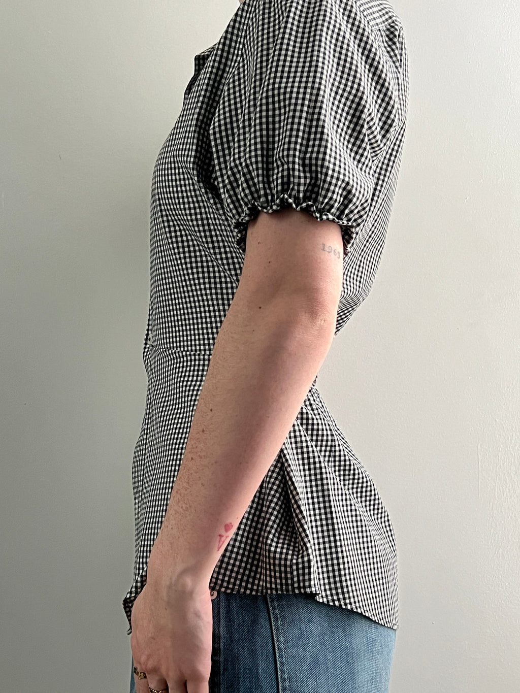 Female wearing a black and white checkered shirt with puff sleeves and jeans.