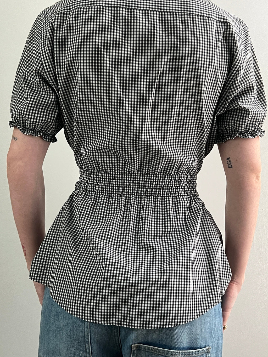 Female wearing a black and white checkered shirt with puff sleeves and jeans.