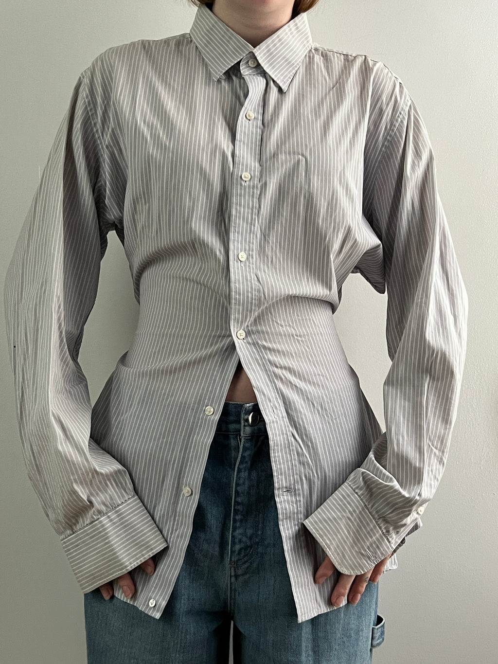 Female wearing a gray striped button down blouse with a cinched elastic back facing front.