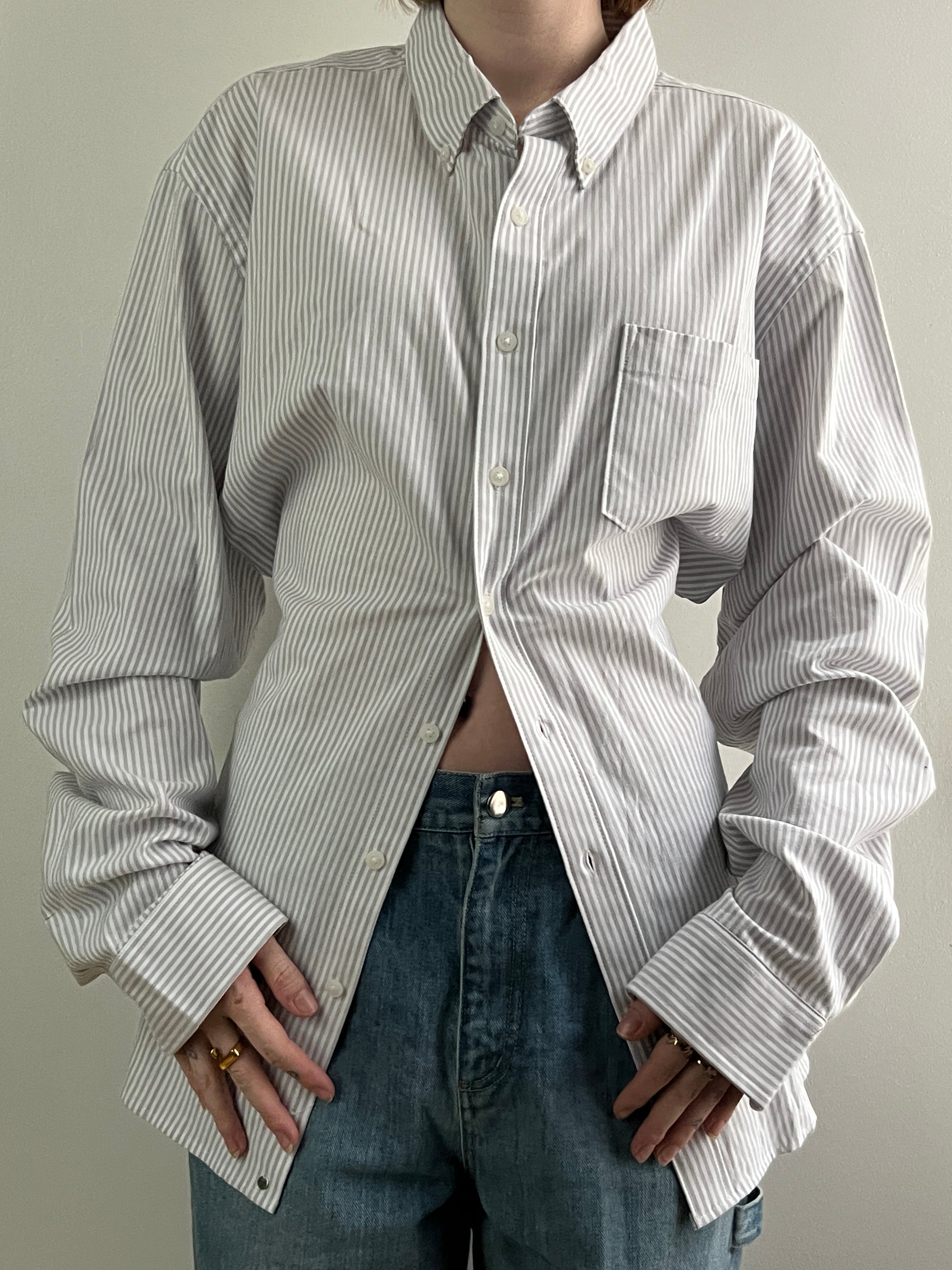 Female wearing a gray striped button down blouse with a cinched elastic back facing front.