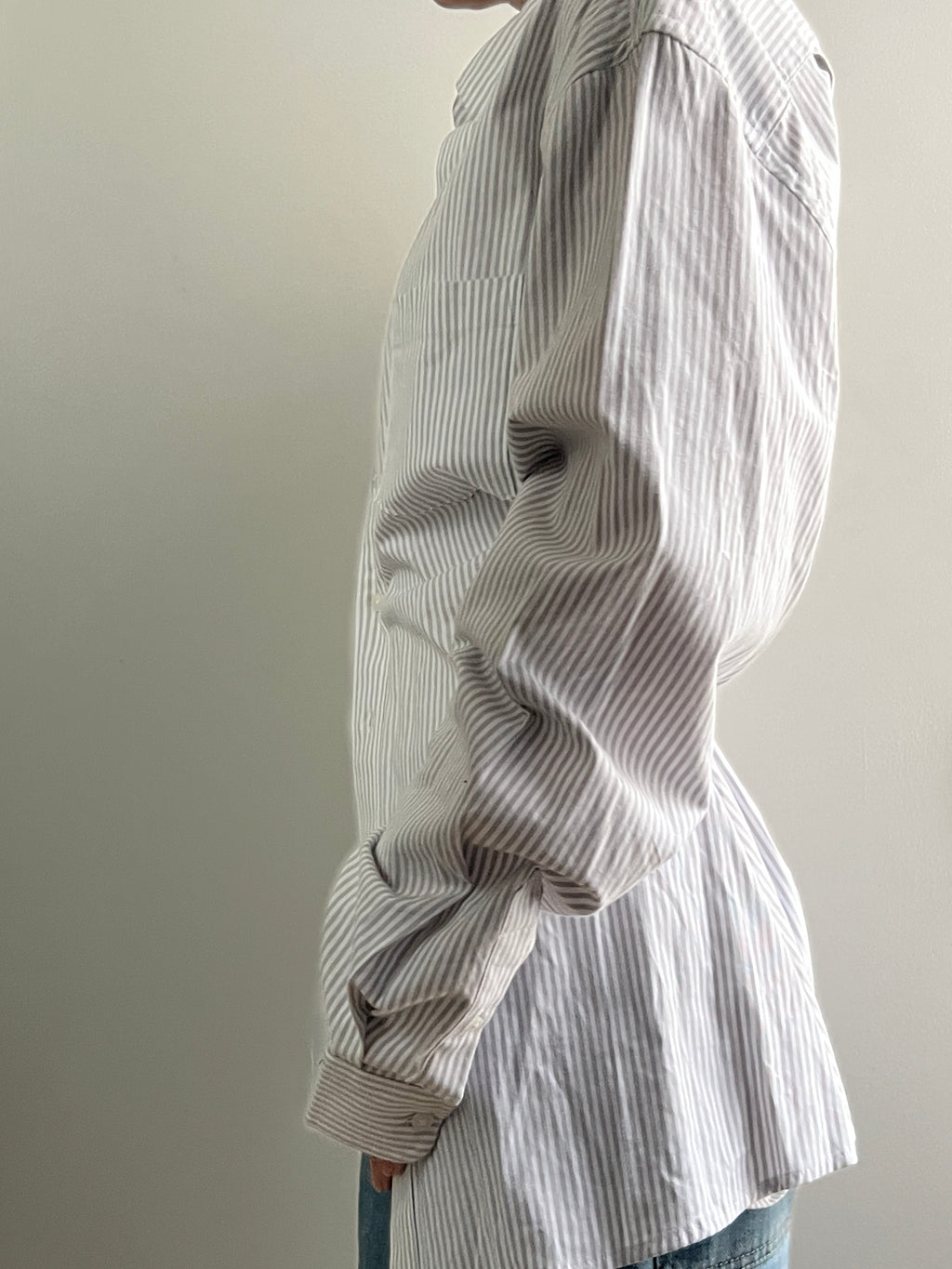 Female wearing a gray striped button down blouse with a cinched elastic back facing left.