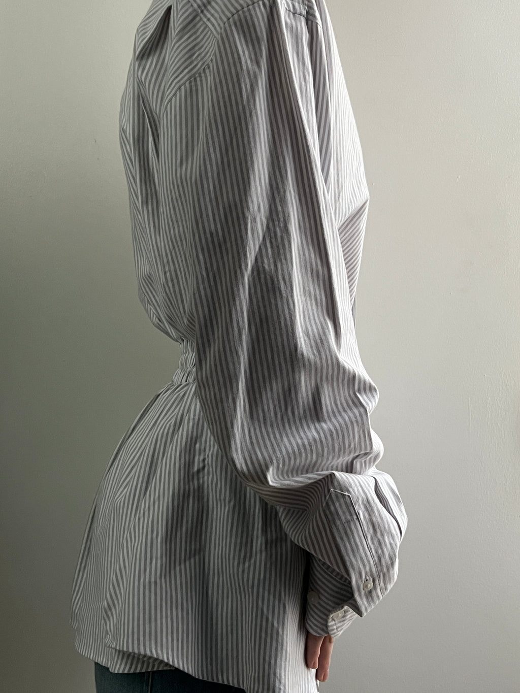 Female wearing a gray striped button down blouse with a cinched elastic back facing right.