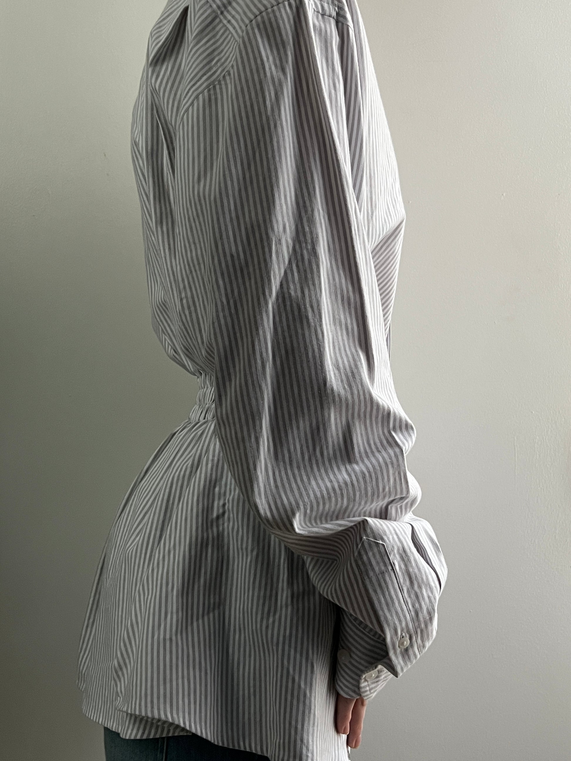 Female wearing a gray striped button down blouse with a cinched elastic back facing right.