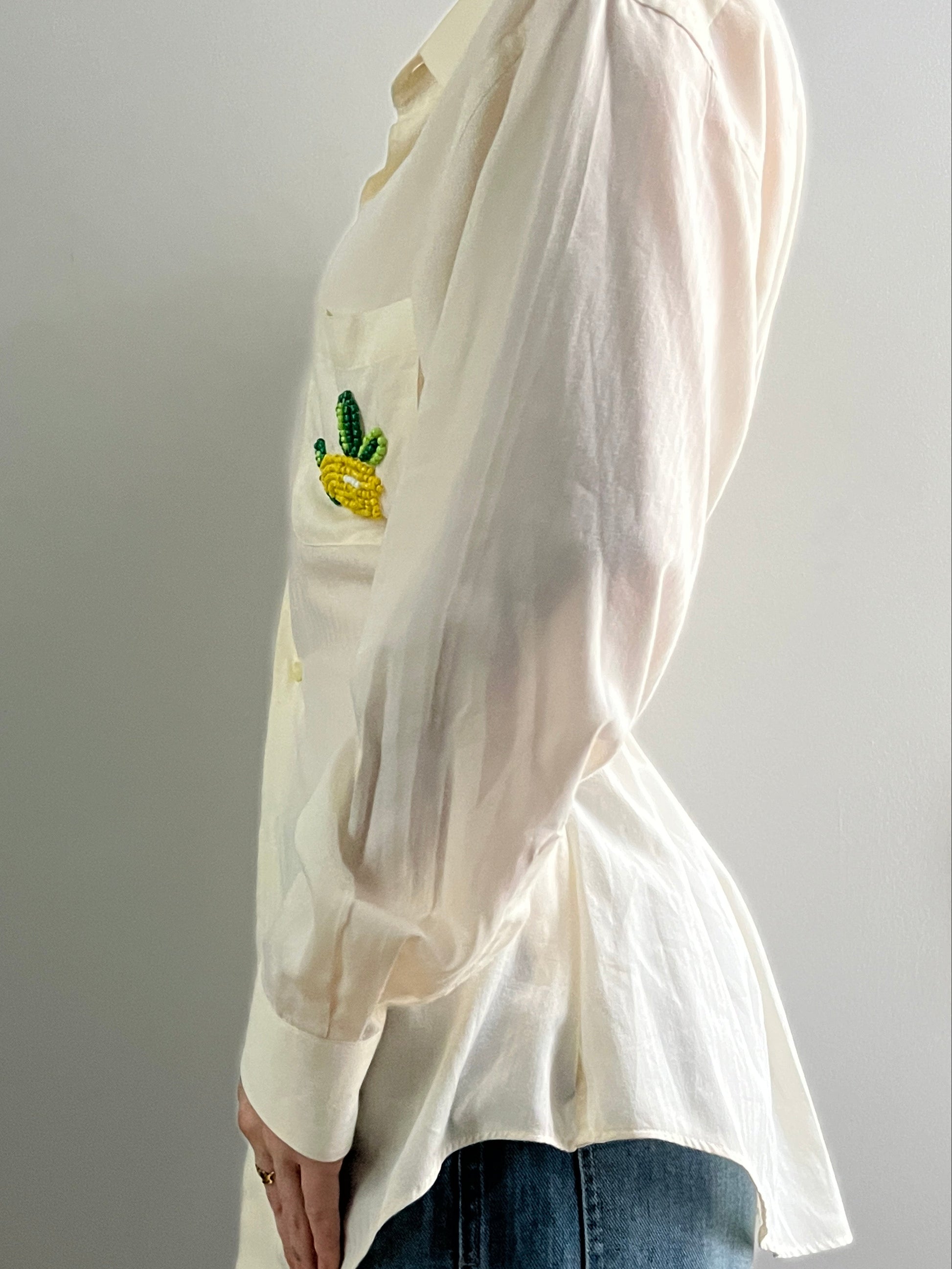 Female wearing a pale yellow button down blouse with a cinched elastic back facing left.