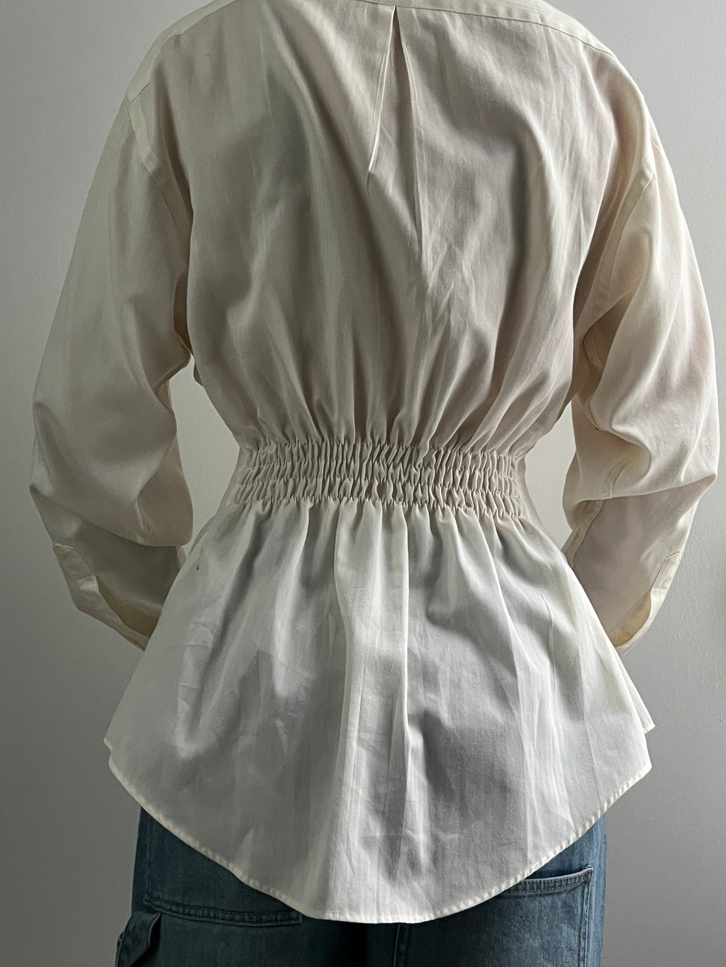 Female wearing a pale yellow button down blouse with a cinched elastic back facing back.