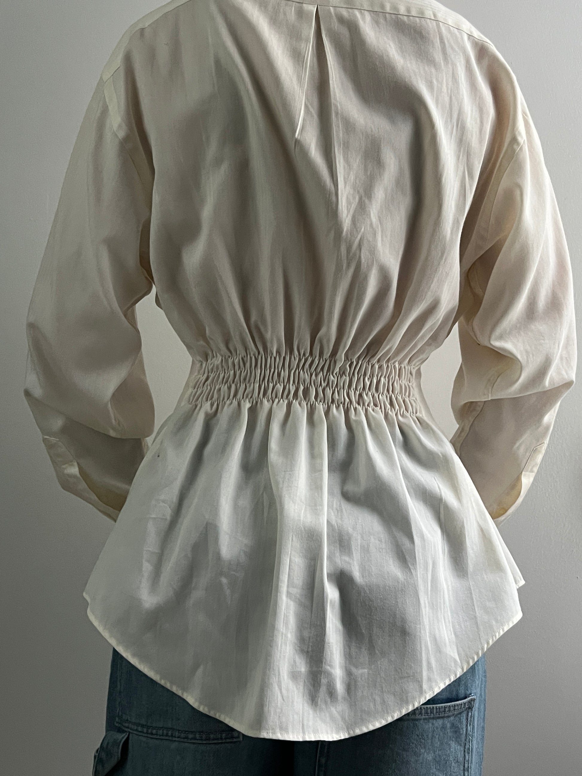Female wearing a pale yellow button down blouse with a cinched elastic back facing back.