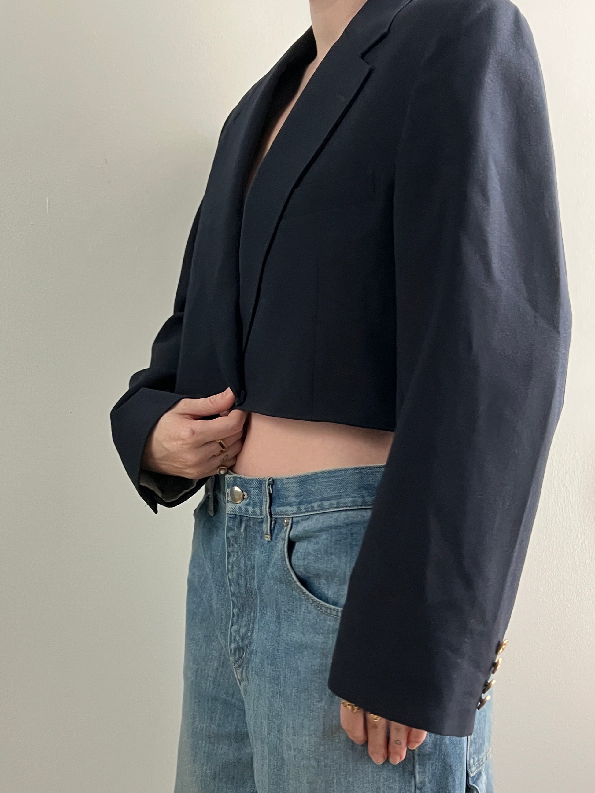 Female wearing a navy cropped blazer over light blue jeans on a neutral background