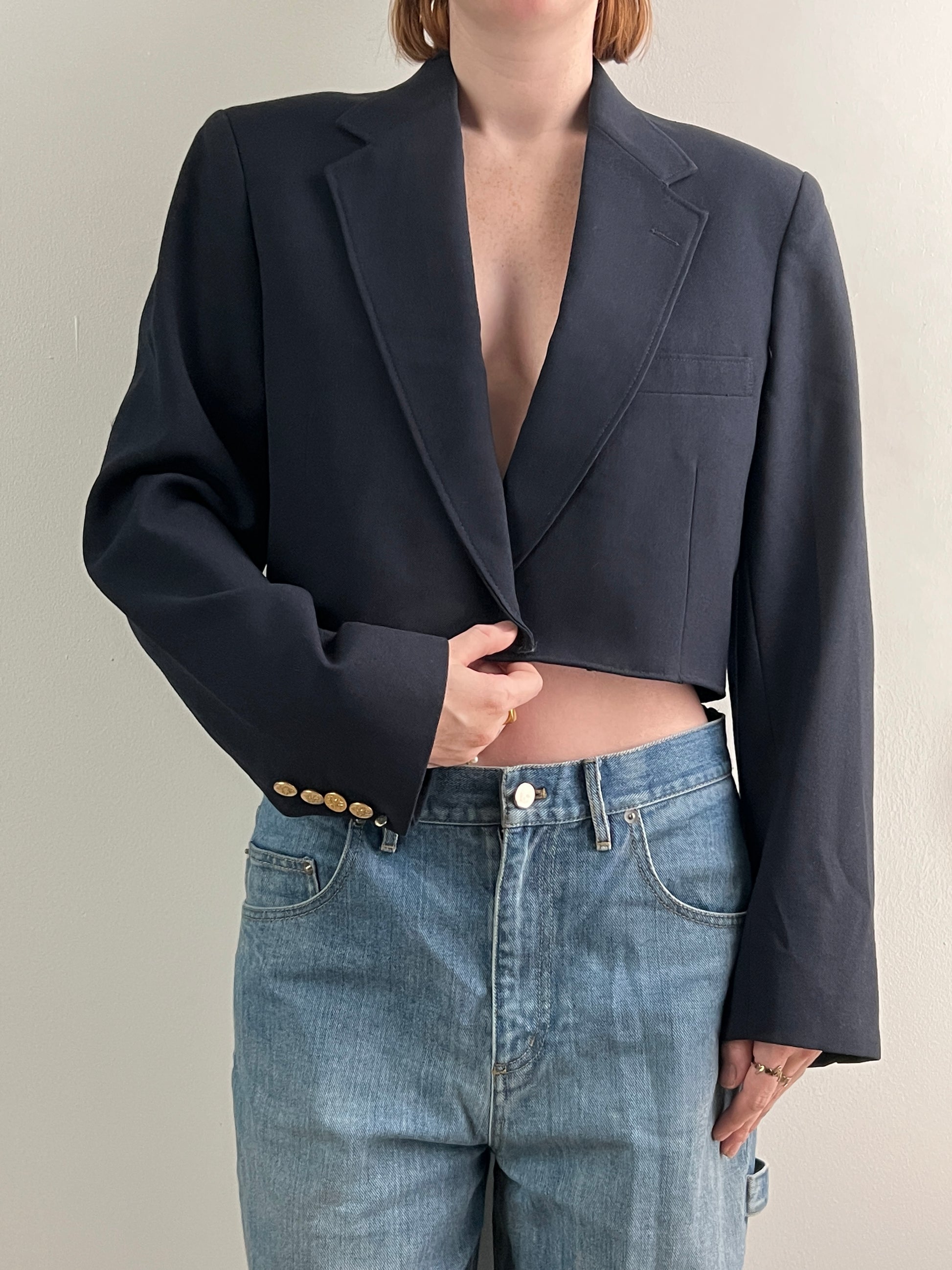 Female wearing a navy cropped blazer over light blue jeans on a neutral background