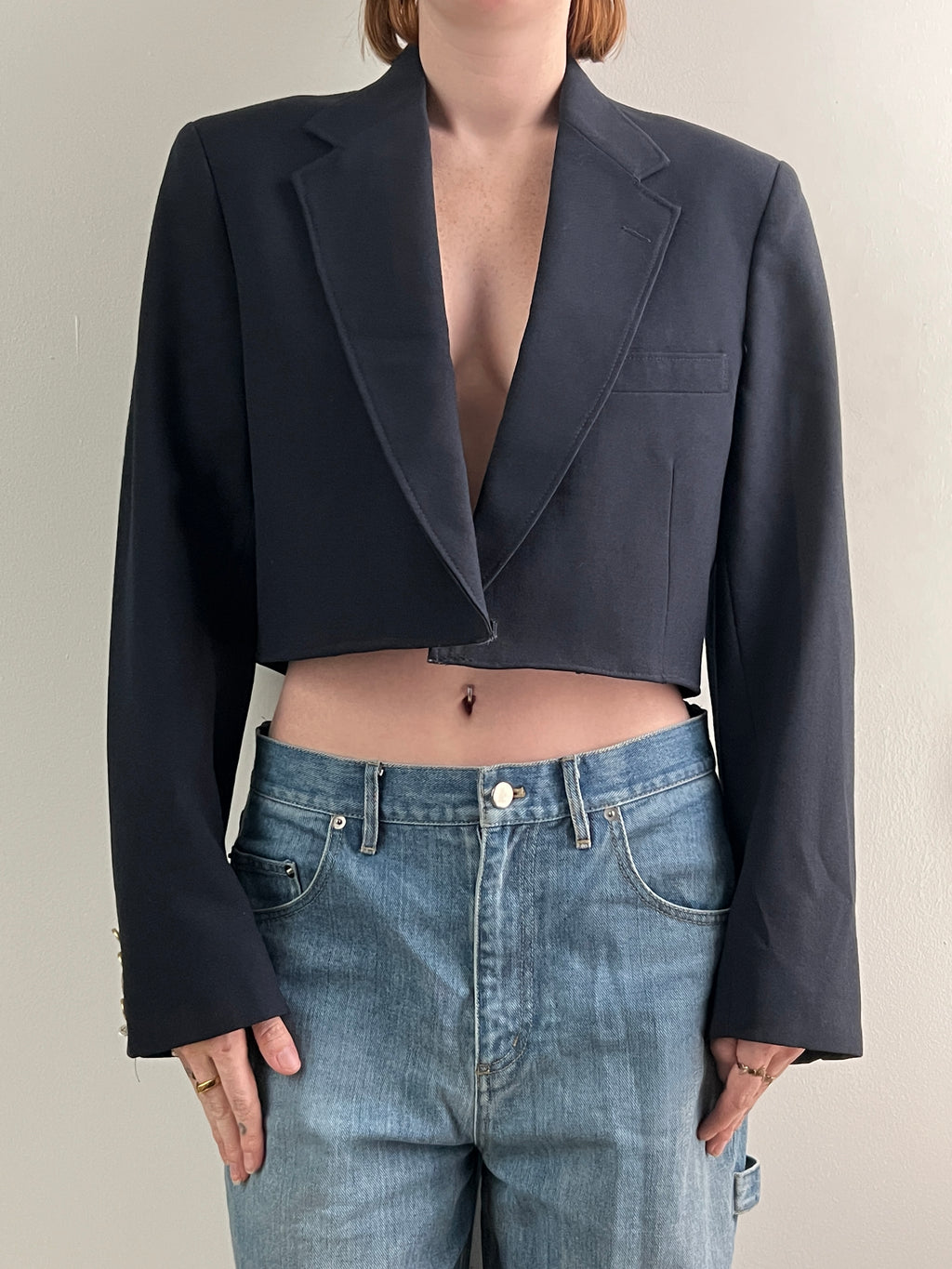 Female wearing a navy cropped blazer over light blue jeans on a neutral background