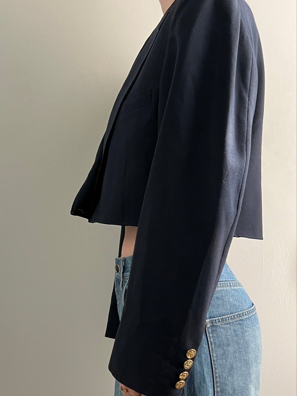 Navy blazer with gold buttons worn with jeans on a neutral background