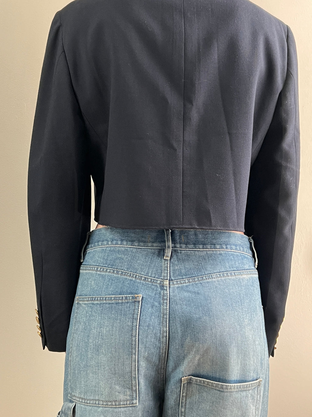 Female wearing a navy cropped blazer over light blue jeans on a beige background
