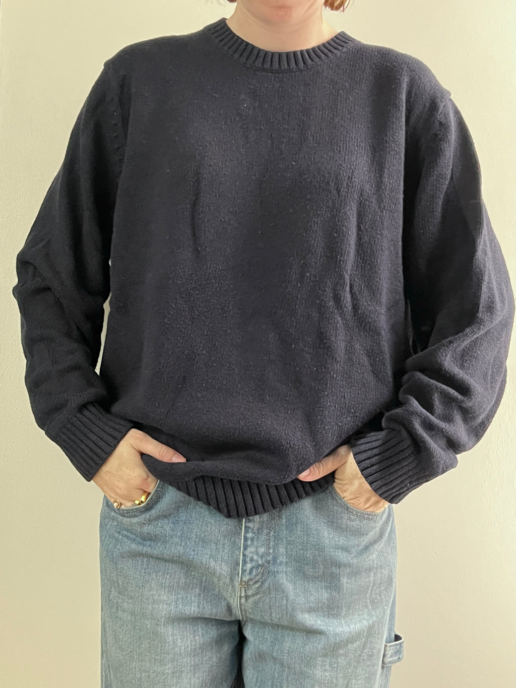 Female wearing a dark navy sweater and light blue jeans on a beige background