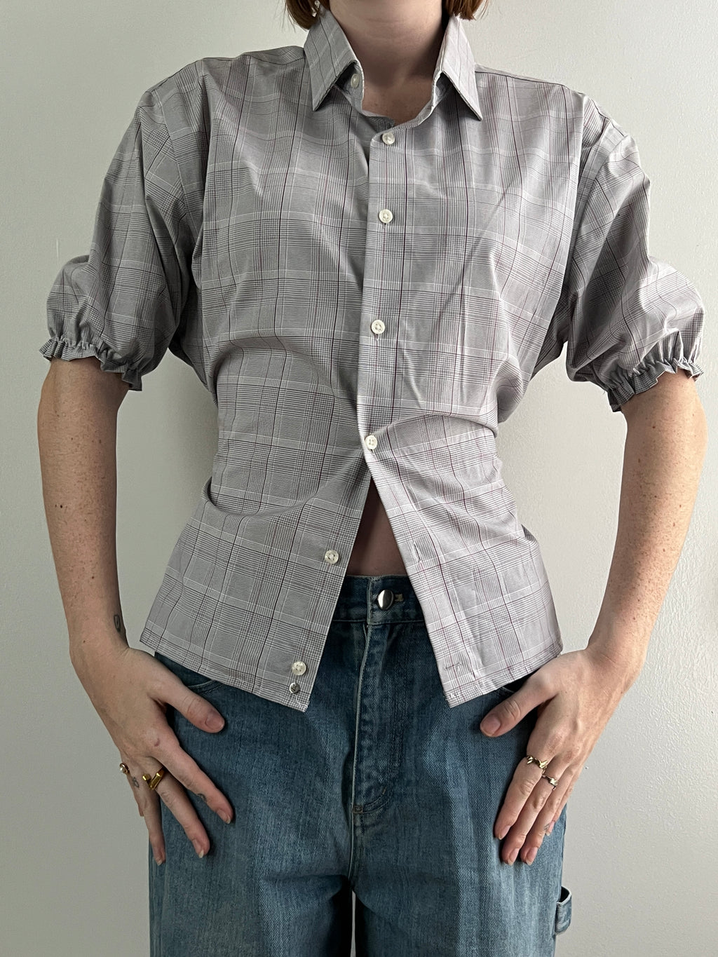 Female wearing a plaid short sleeve puff sleeve button down blouse with a cinched back facing front.