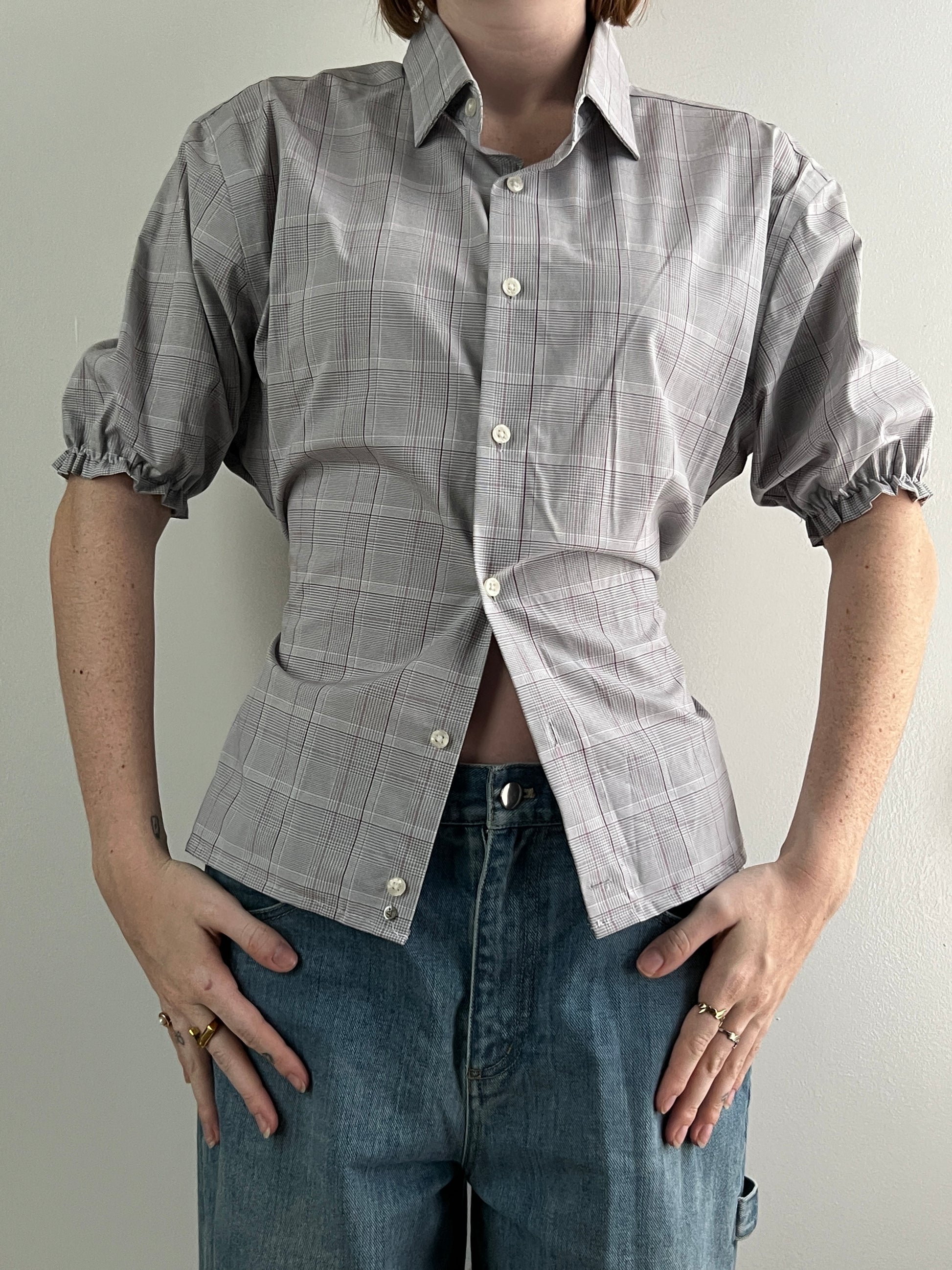 Female wearing a plaid short sleeve puff sleeve button down blouse with a cinched back facing front.